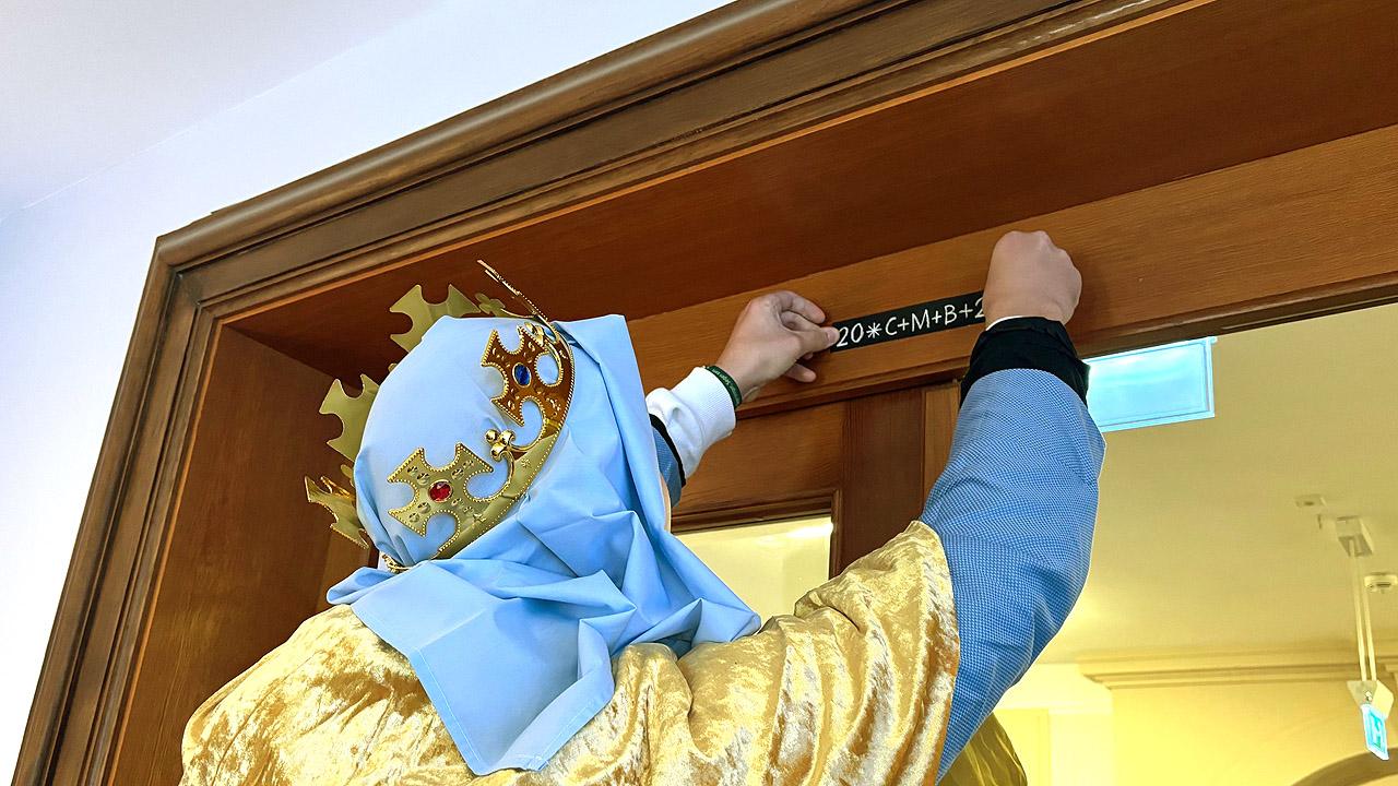 Sternsinger Verkleideter König bringt Segens-Symole über einem Türrahmen an