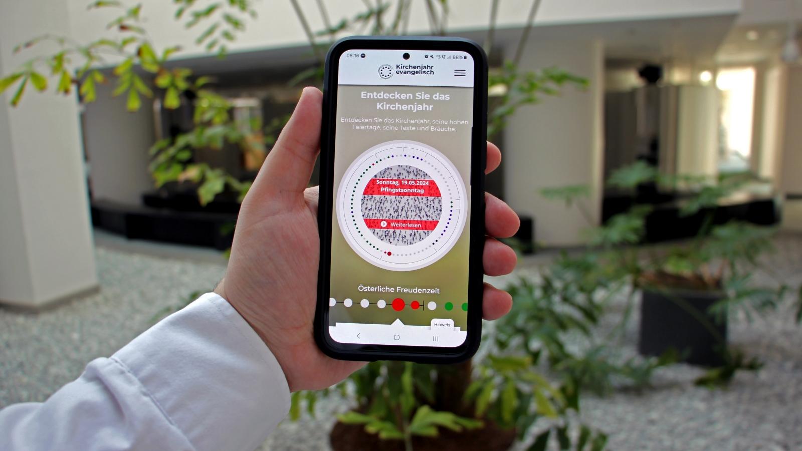 Smartphone App Kirchenjahr 2024 Jemnad hält ein Smartphone in der Hand, es ist die App zu sehen.