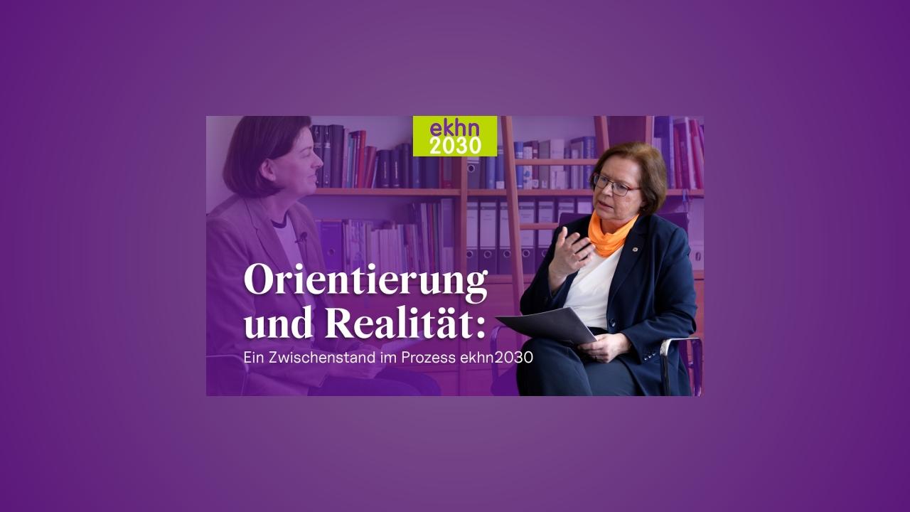 Zwei Frauen im Gespräch in einem Büro mit Bücherregalen; Einblendung: ‚Orientierung und Realität – Zwischenstand im Prozess ekhn2030‘.