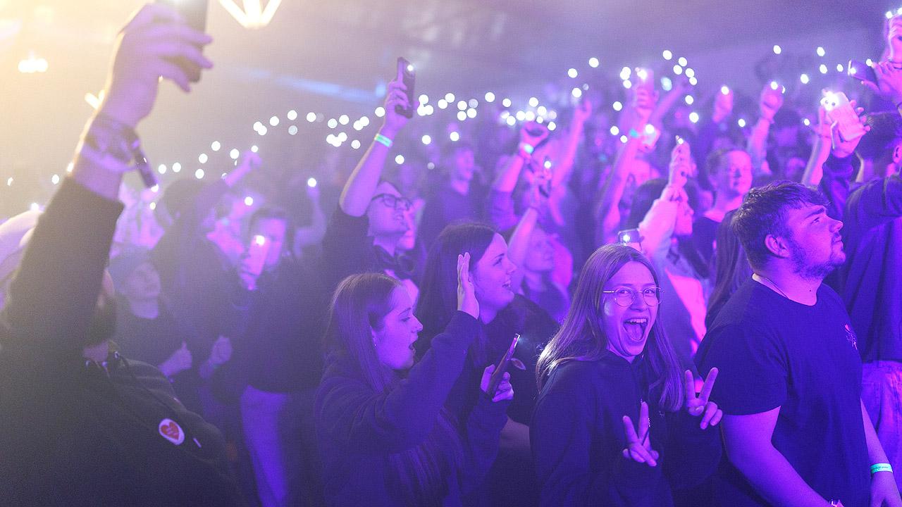 Jugendkirchentag Eröffnungsabend Jugendliche in violettes Licht getaucht, im Hintergrund Lichter, vorne eine gut gelaunte junge Frau