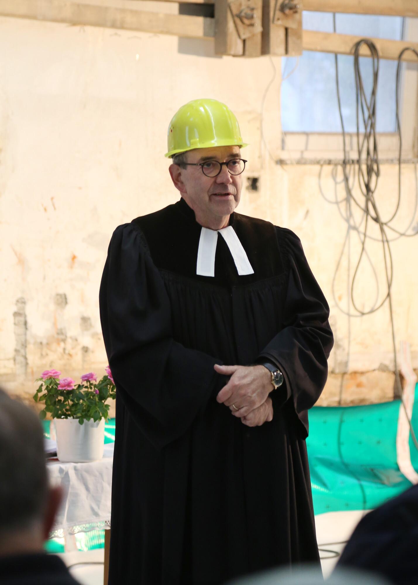 Pfarrer mit Bauhelm Pfarrer in schwarzem Talar und Beffchen mit gelbem Bauhelm