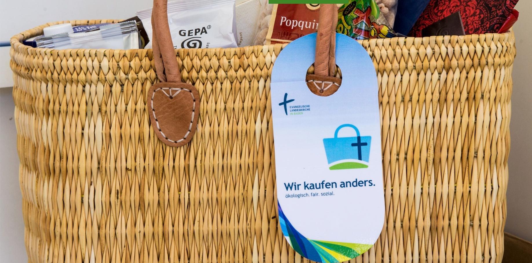 An einem vollen Einkaufskorb aus Bast hängt ein Schild: Wir kaufen anders. öko. fair. sozial.