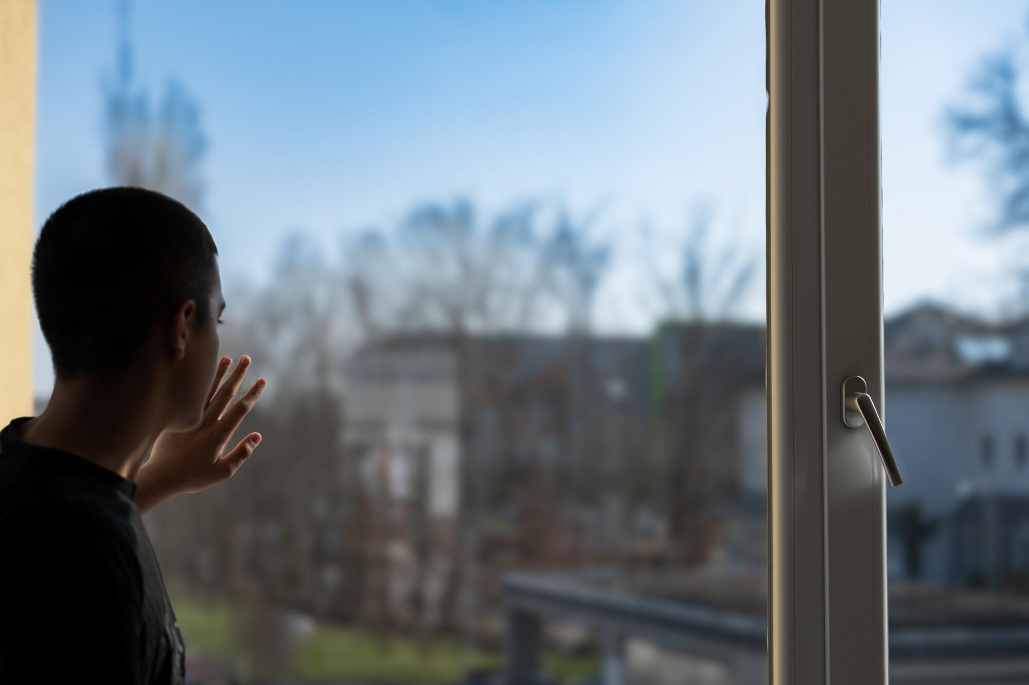 Junger Mann Fenster Junger Mann schaut aus dem Fenster