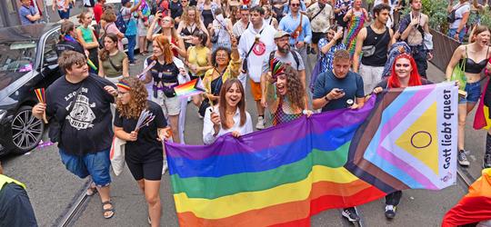 Jugendliche tragen eine große Flagge mit der Aufschrift: "Gott liebt queer."
