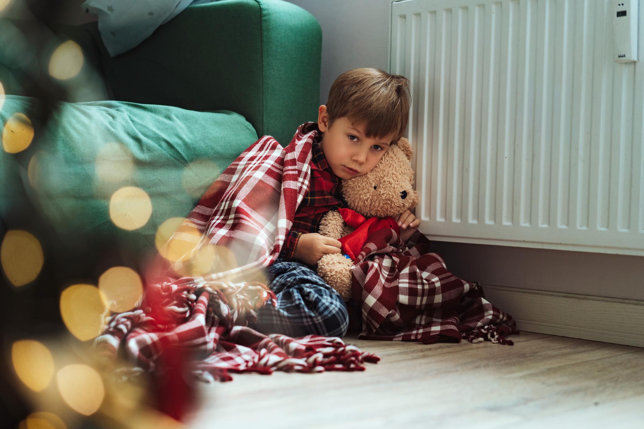 Wärmewinter Frierendes Kind sitzt mit Teddy auf dem Boden an der Heizung.