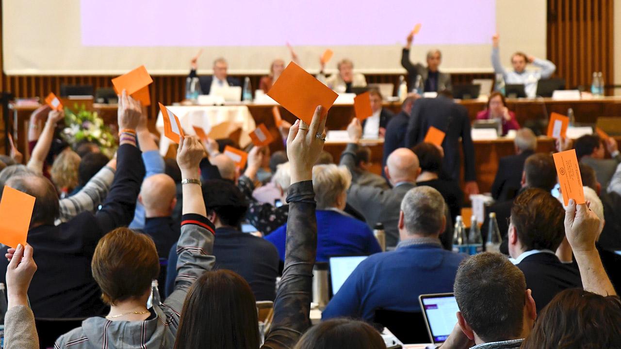 Synodenbeschluss Synodale heben einen orangenen Zettel hoch