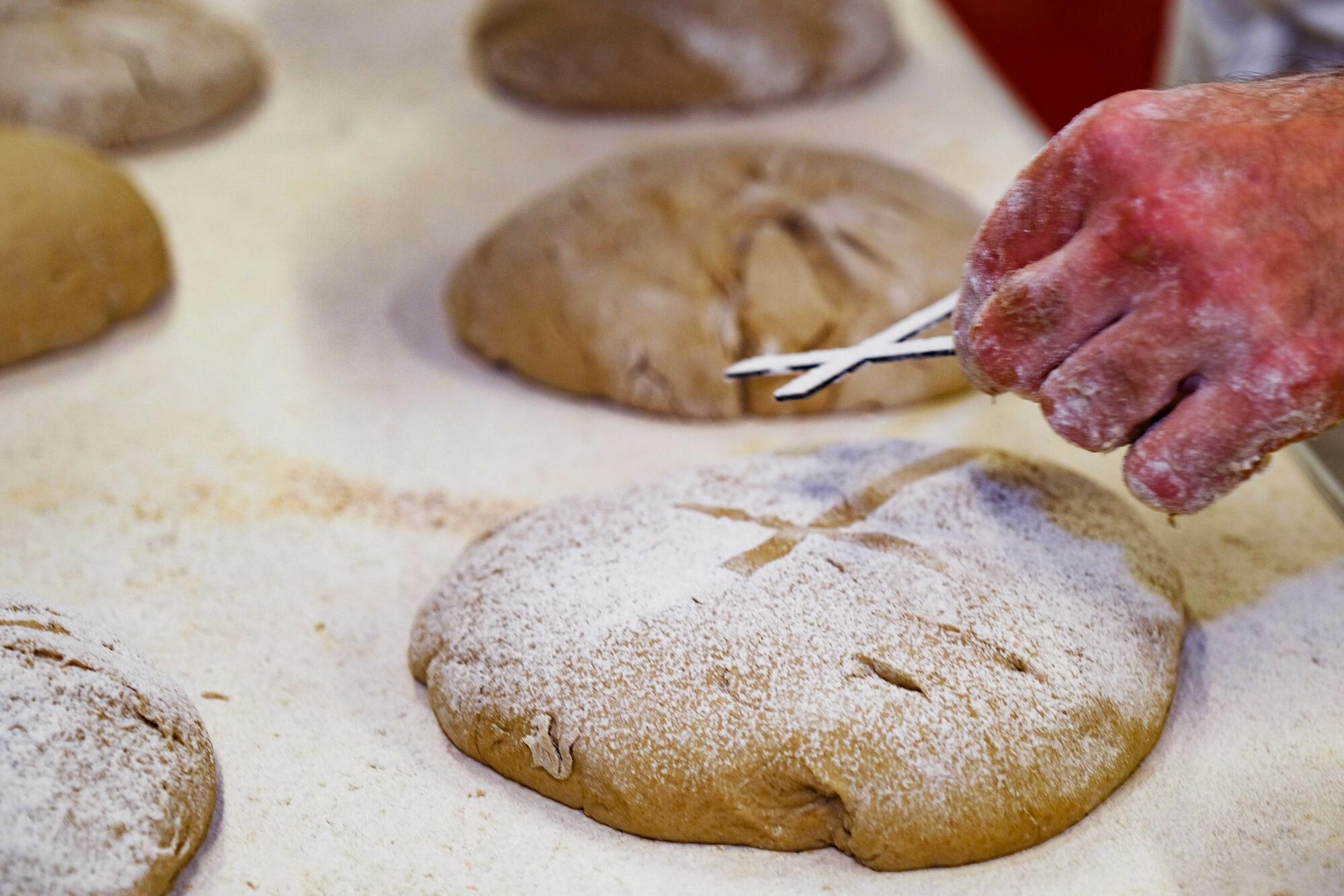 Aktion 5000 Brote - Brot für die Welt_002 In einer Bäckerei wird Brot gebacken für die Aktion "5.000 Brote - Brot für die Welt". Im Vordergrund ein Brot und eine Hand, die ein Kreuz hält, um das Kreuz als Motiv auf das Brot zu bringen.