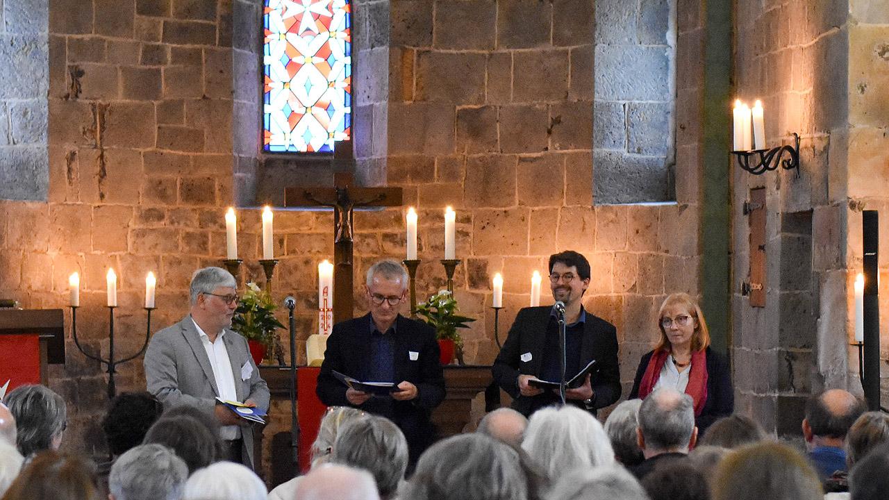 Vier Menschen sitzen im Altarraum, es brennen Kerzen auf hohen Kerzenständern