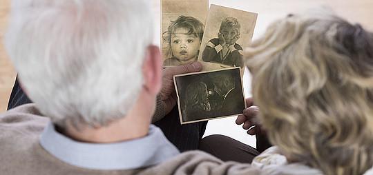Zwei Senioren schauen auf verschiedene alte Kinderfotos
