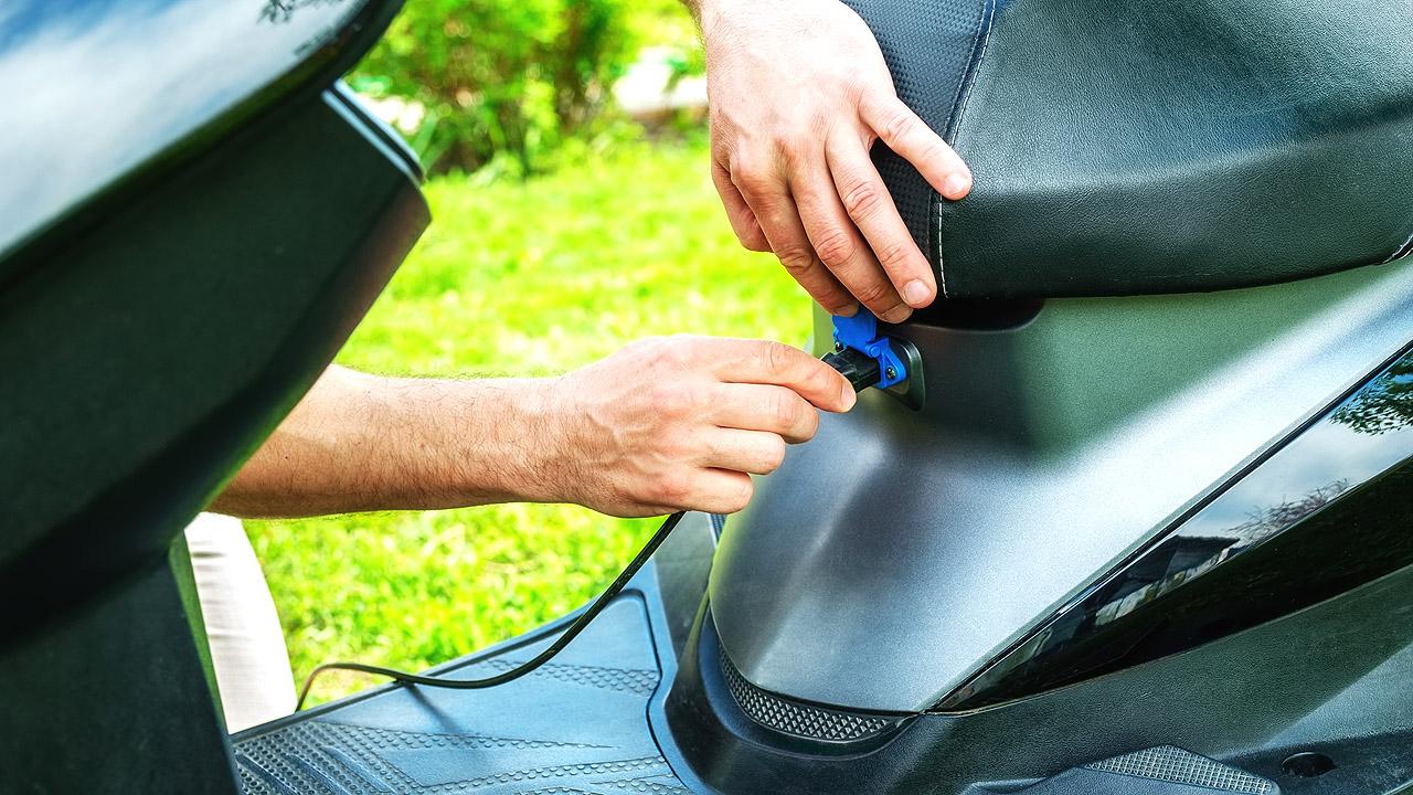 Elektroroller Eine männliche Hand steckt den Ladestecker in einen Motorradroller