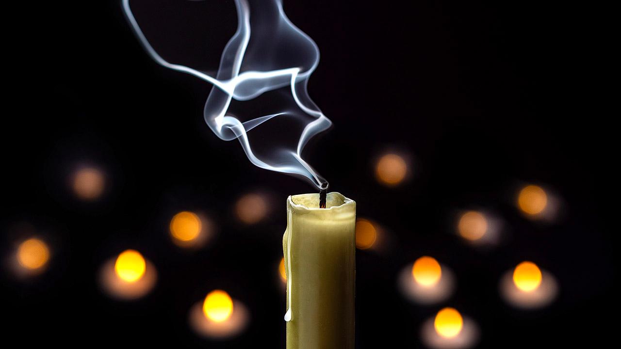 Gedenken Vorne eine erloschene Kerze, im Hintergrund Lichter