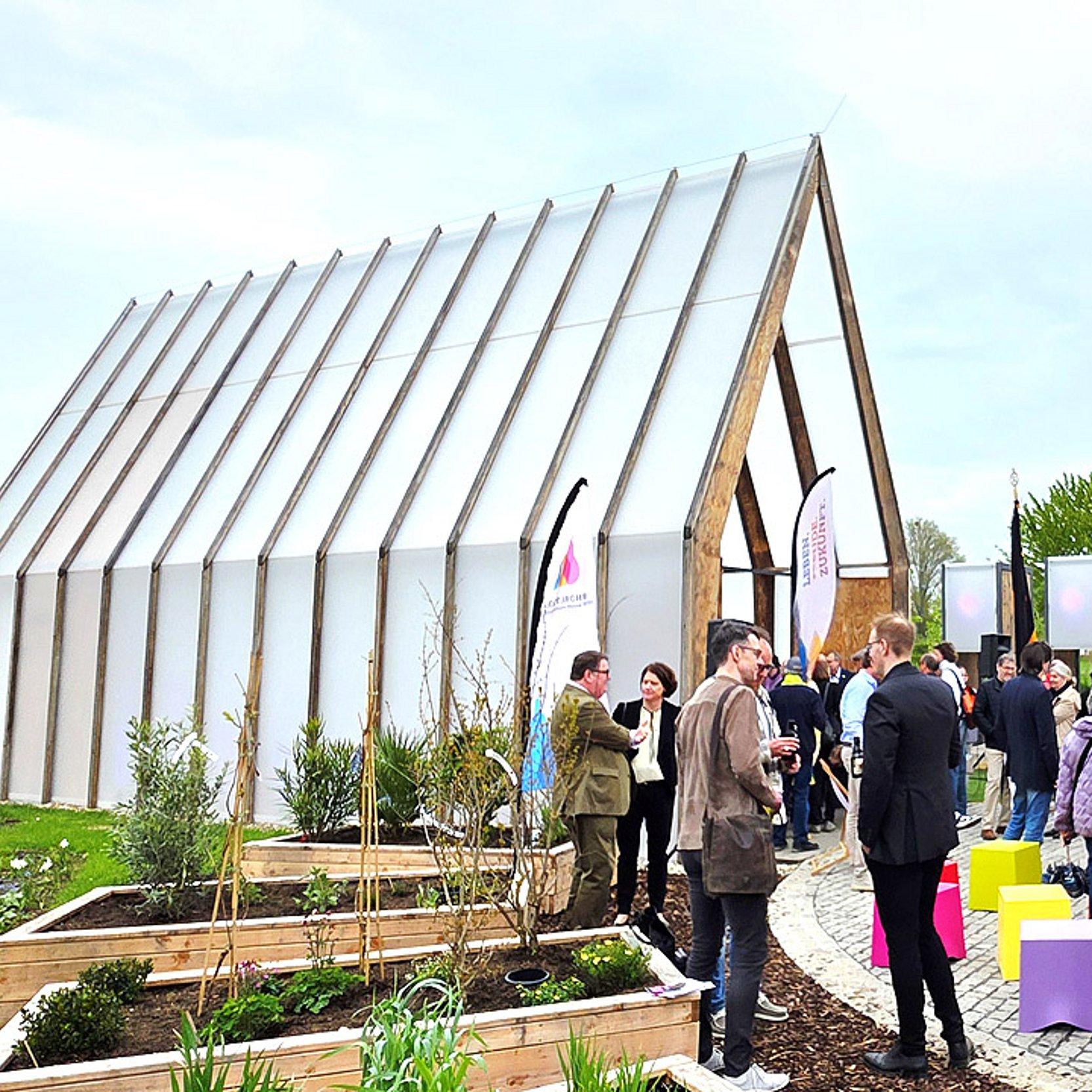 Lichtkirche Kleine Kirche mit milchigem Plexiglas, davor Hochbeete und Publikum