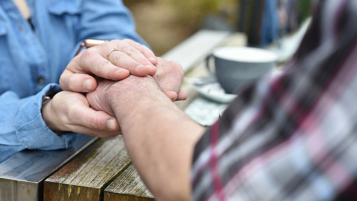 im Fokus stehen zwei Hände, die dem gegenüber auf seine Hand aufliegen