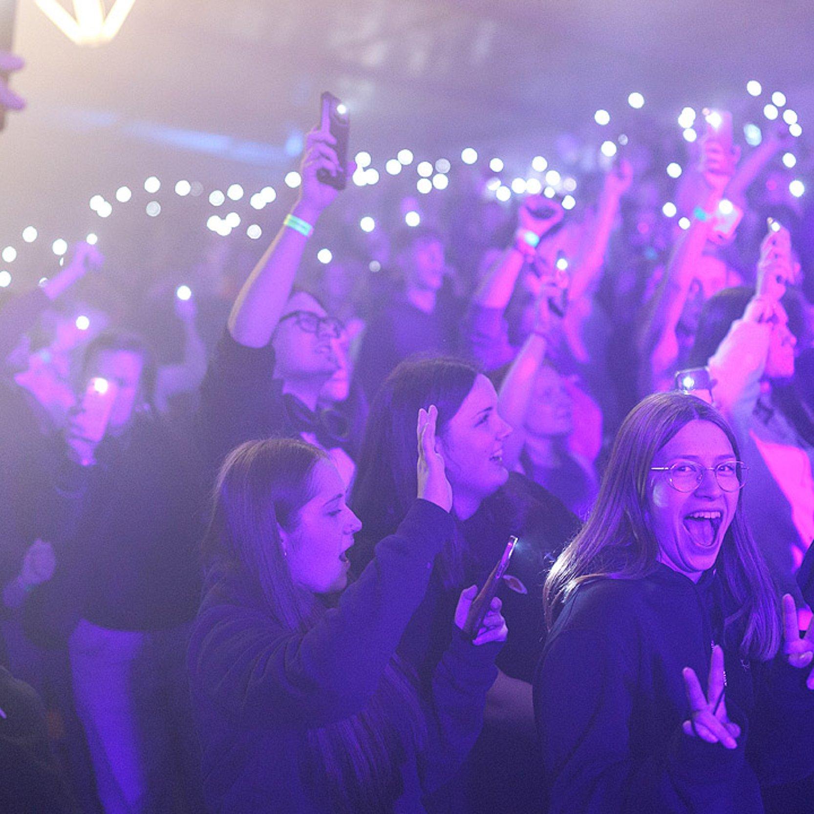 Jugendkirchentag Eröffnungsabend Jugendliche in violettes Licht getaucht, im Hintergrund Lichter, vorne eine gut gelaunte junge Frau