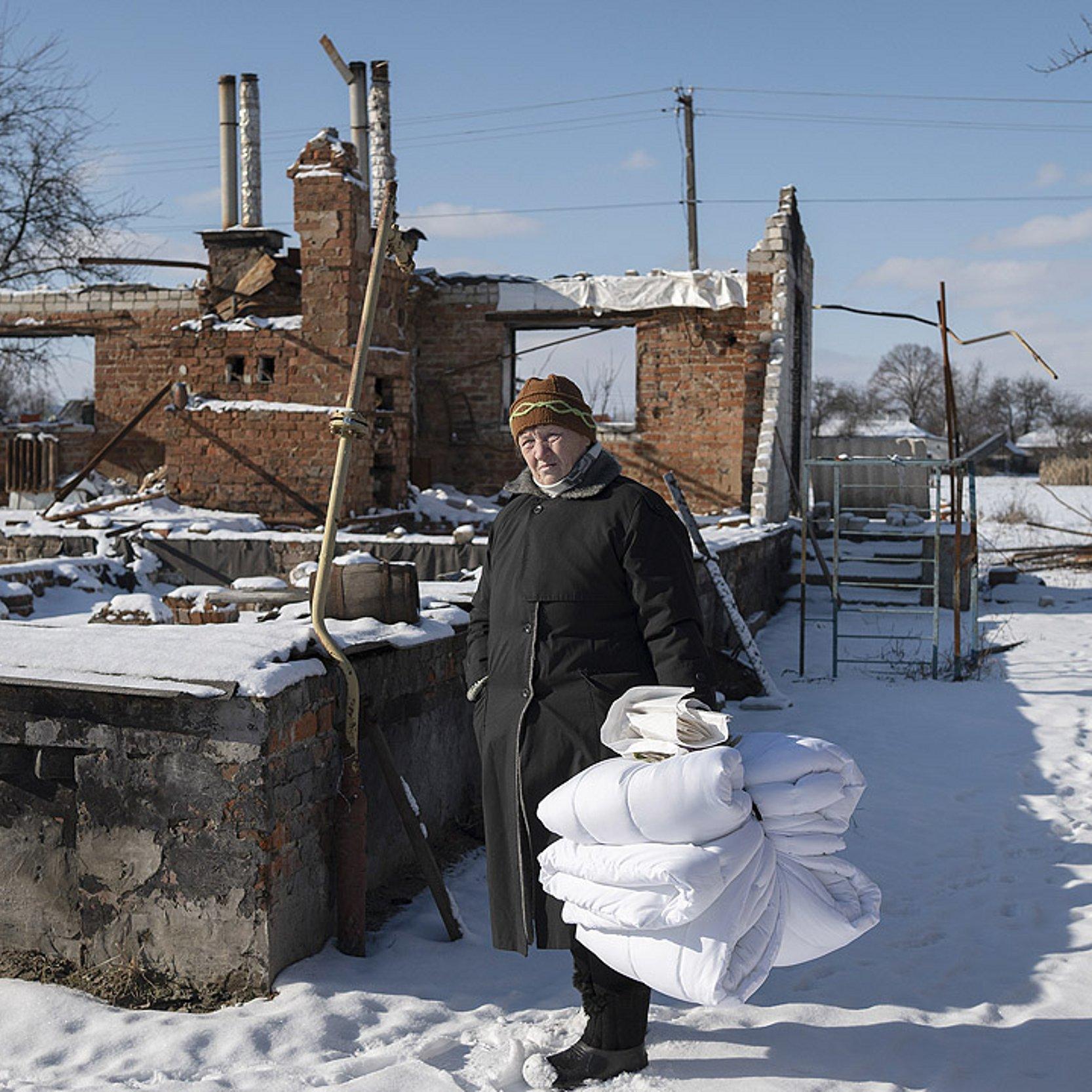 Winterhilfe für die Ukraine Frau mit Bettdecken vor einer Haus-Ruine