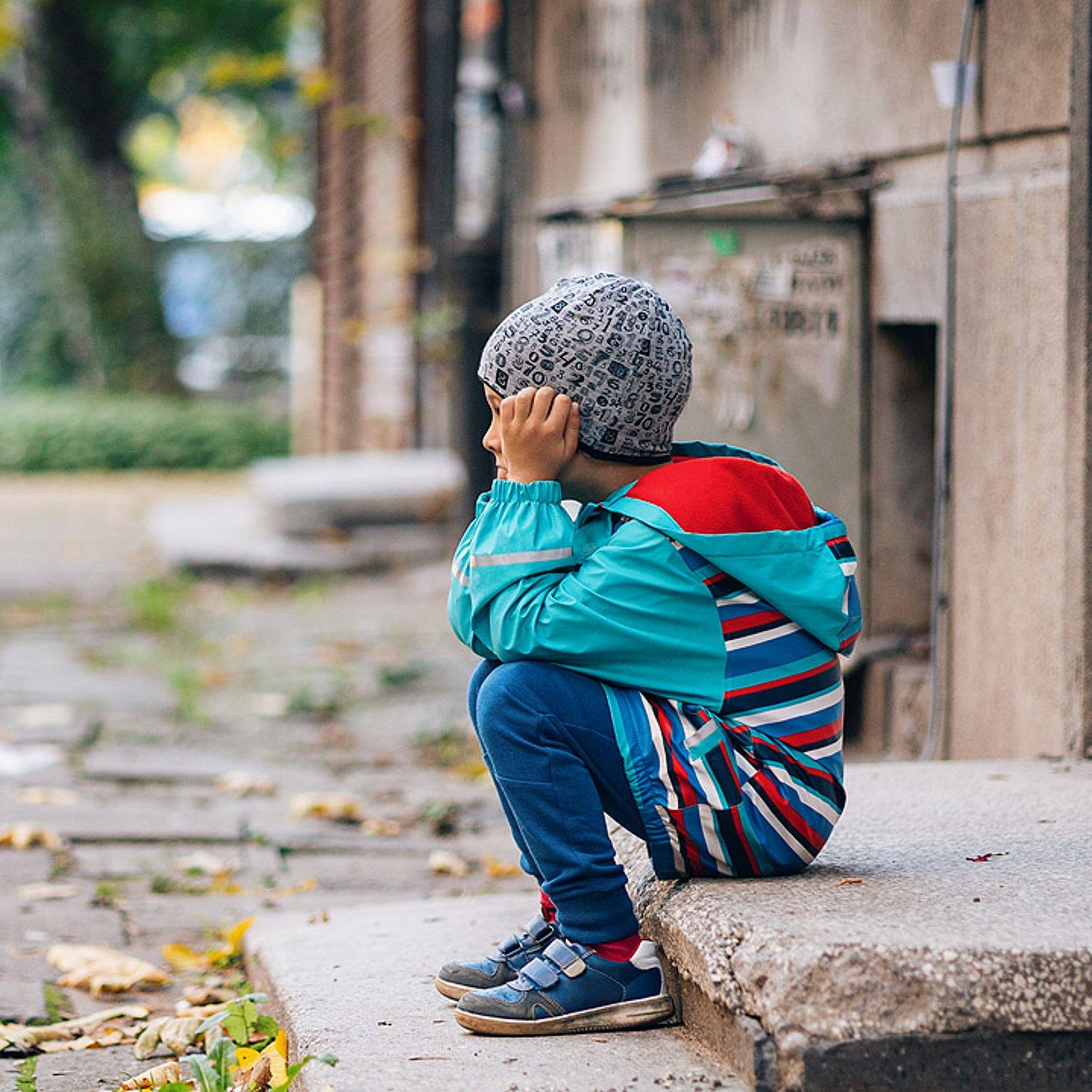 Junge Ein Junge sitzt auf einem Türabsatz an einer Straße und hält den Kopf in den Händen verborgen