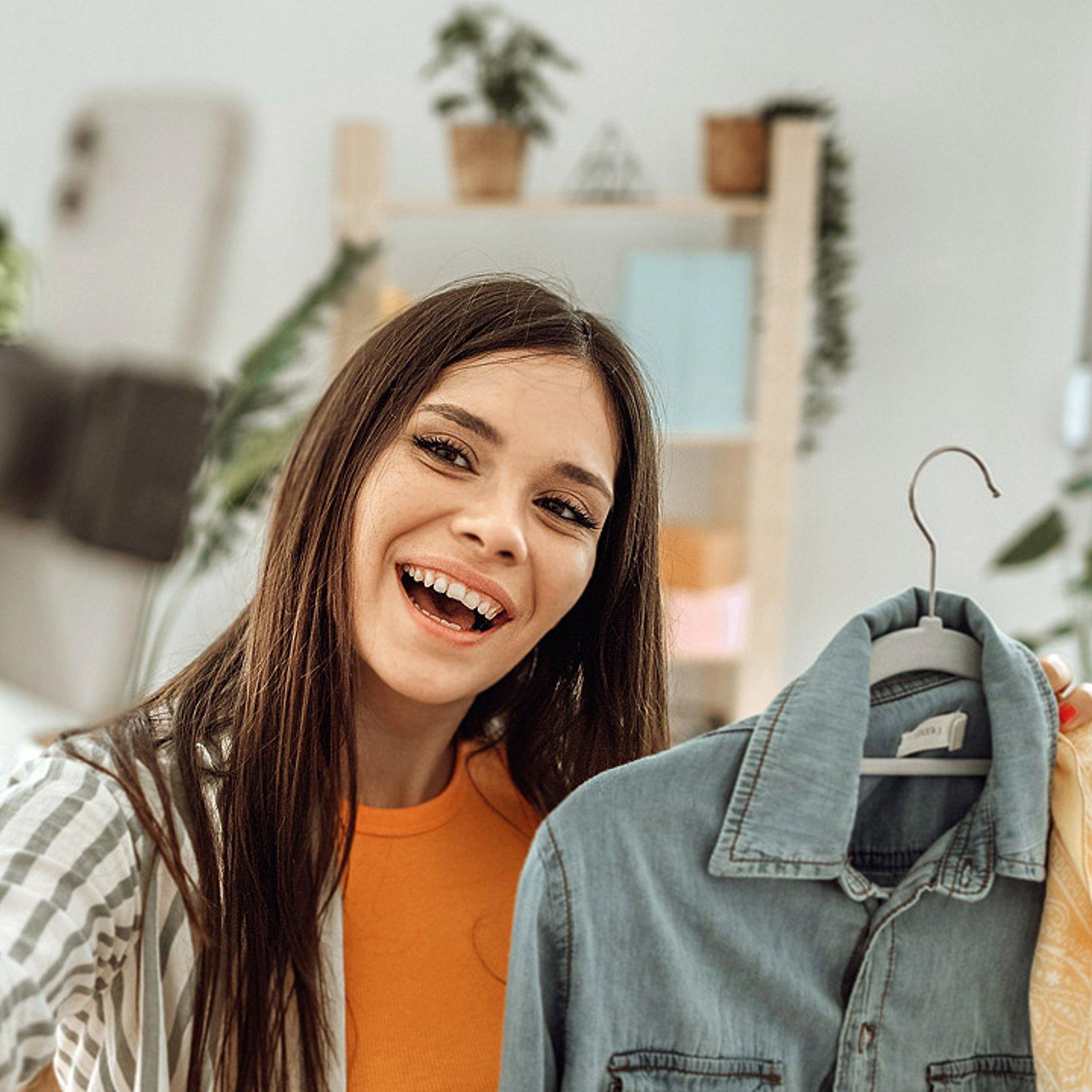 Kleiderschrank ausmisten Eine junge Frau hält ein dunkles Jeans-Männerhemd in der Hand und macht von der Szene ein Selfie