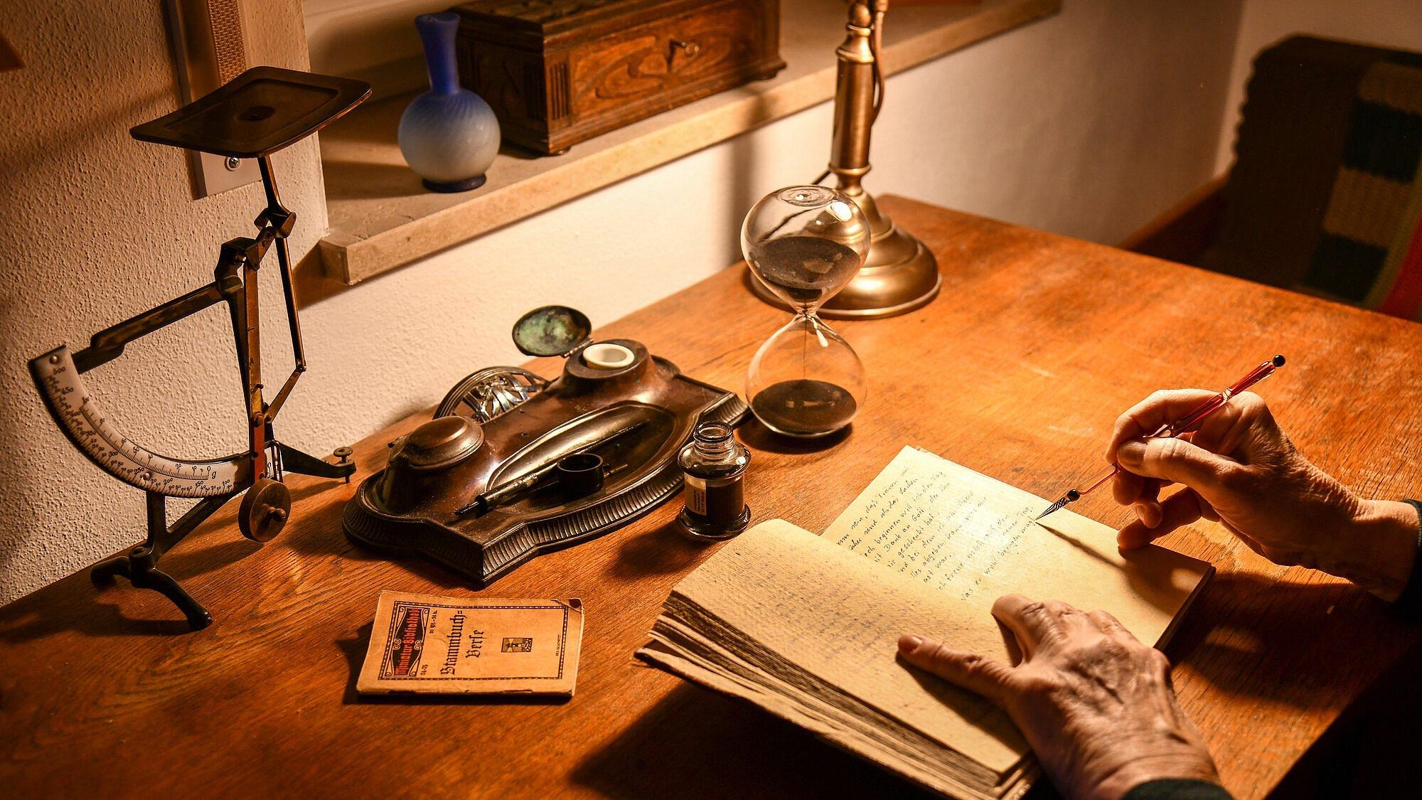 Abendlicher Tagebucheintrag, alter Schreibtisch mit alten Schreibgeräten und eine alte Hand nimmt Eintragungen in ein Tagebuch vor