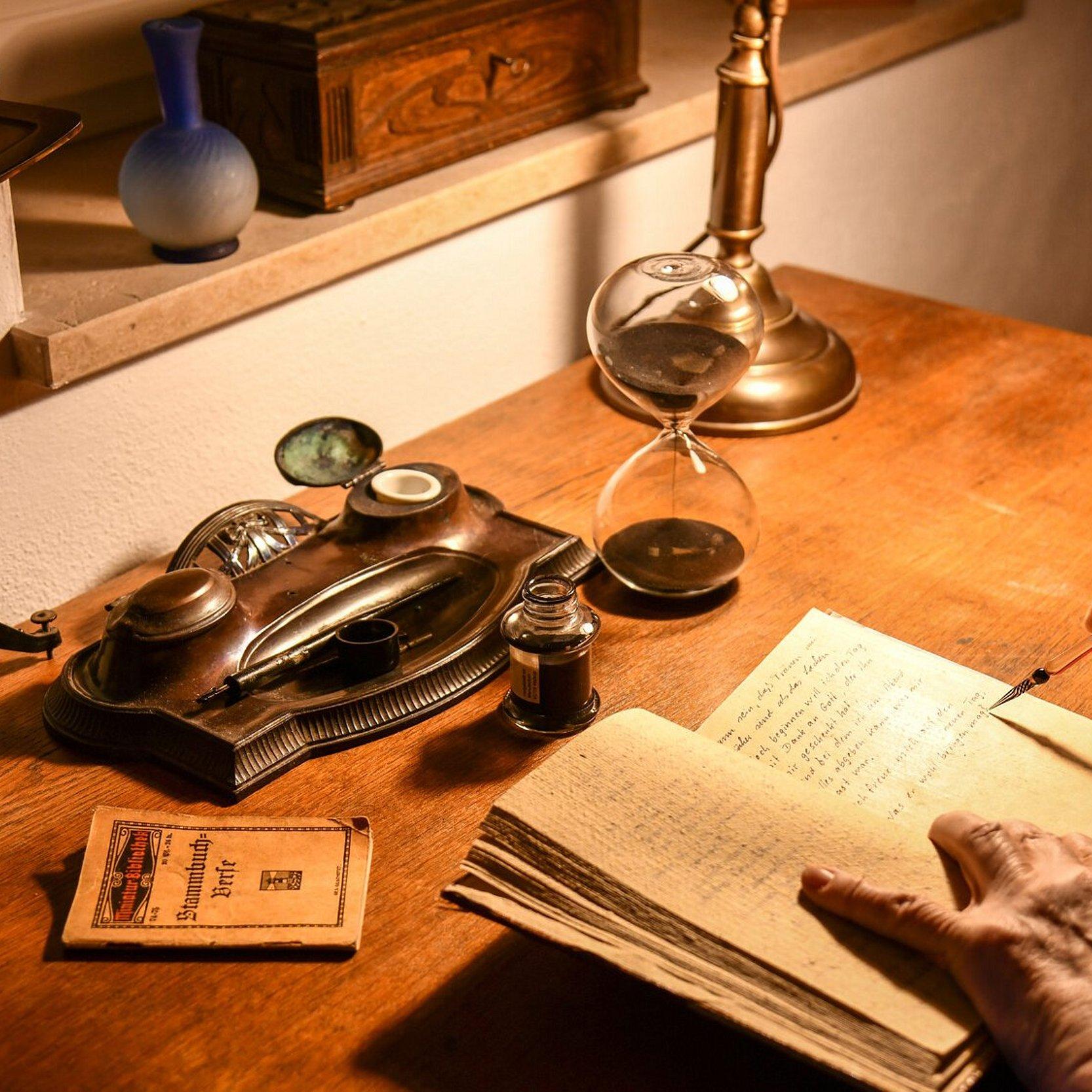 Abendlicher Tagebucheintrag, alter Schreibtisch mit alten Schreibgeräten und eine alte Hand nimmt Eintragungen in ein Tagebuch vor