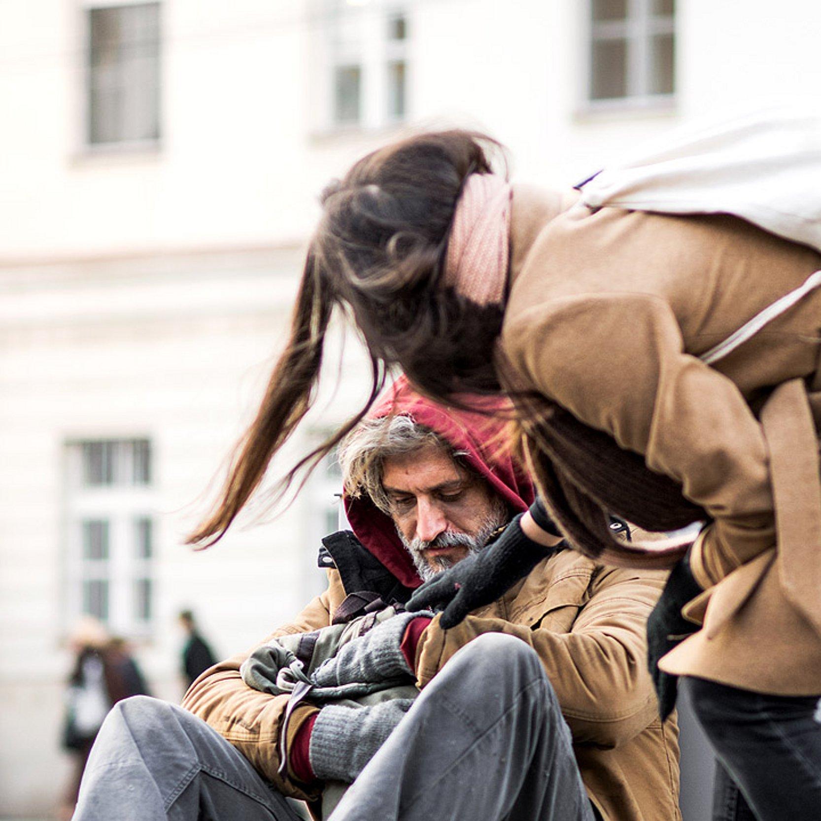 Obdachloser Passantin spendet einem obdachlosen Mann etwas