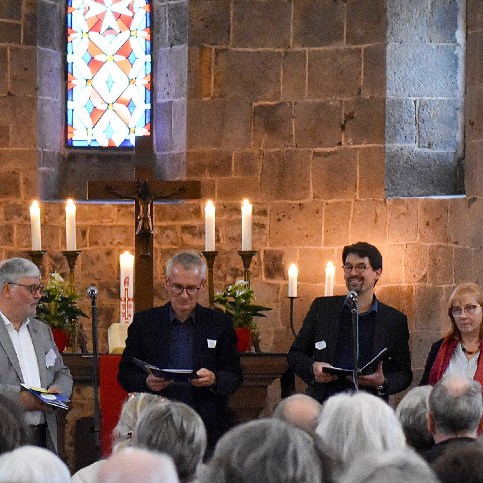 Spirituelle Kirche 2030 Vier Menschen sitzen im Altarraum, es brennen Kerzen auf hohen Kerzenständern