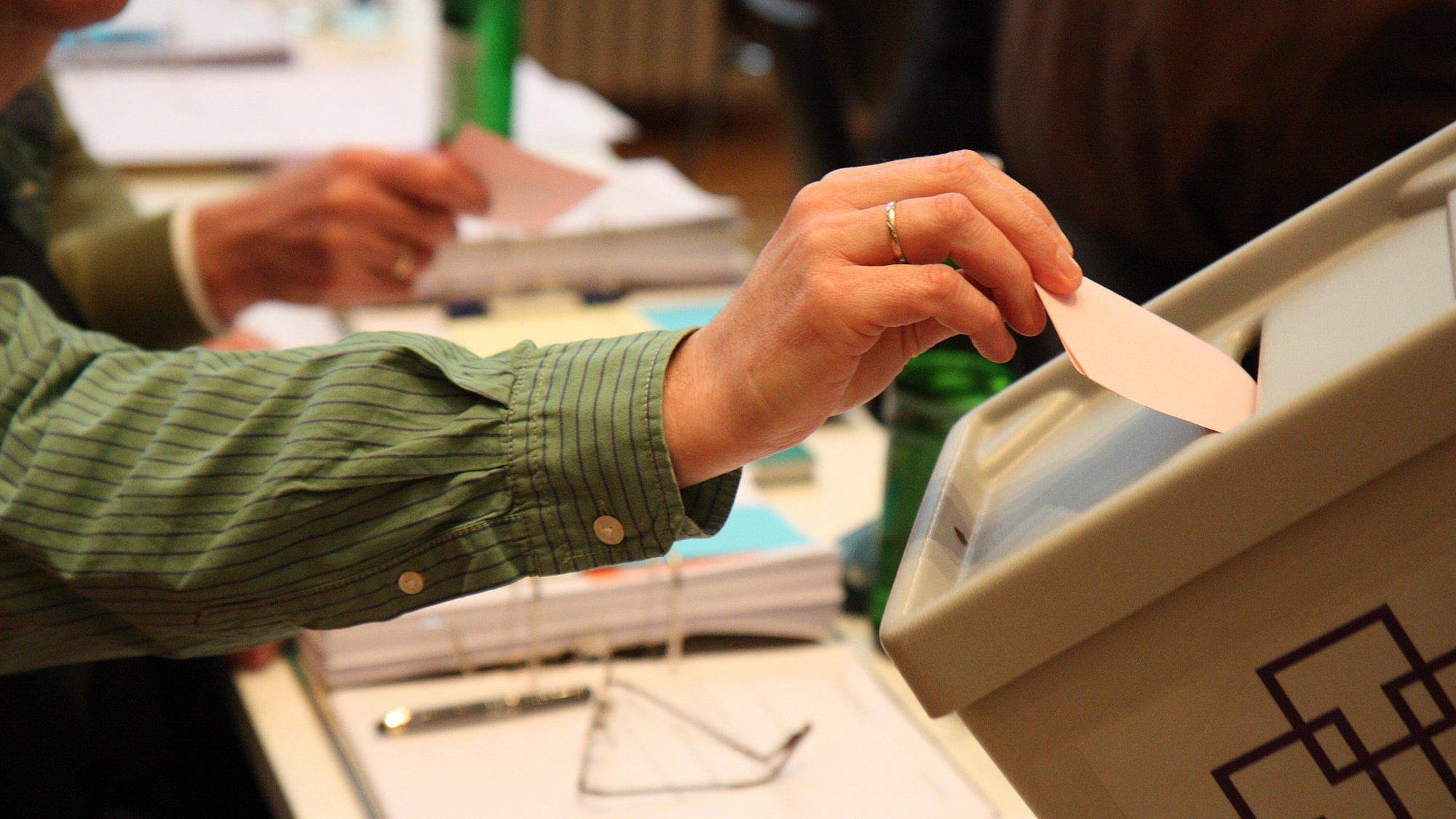 Eine Hand steckt einen Wahlzettel in eine Wahlurne mit einem Logo der EKHN..