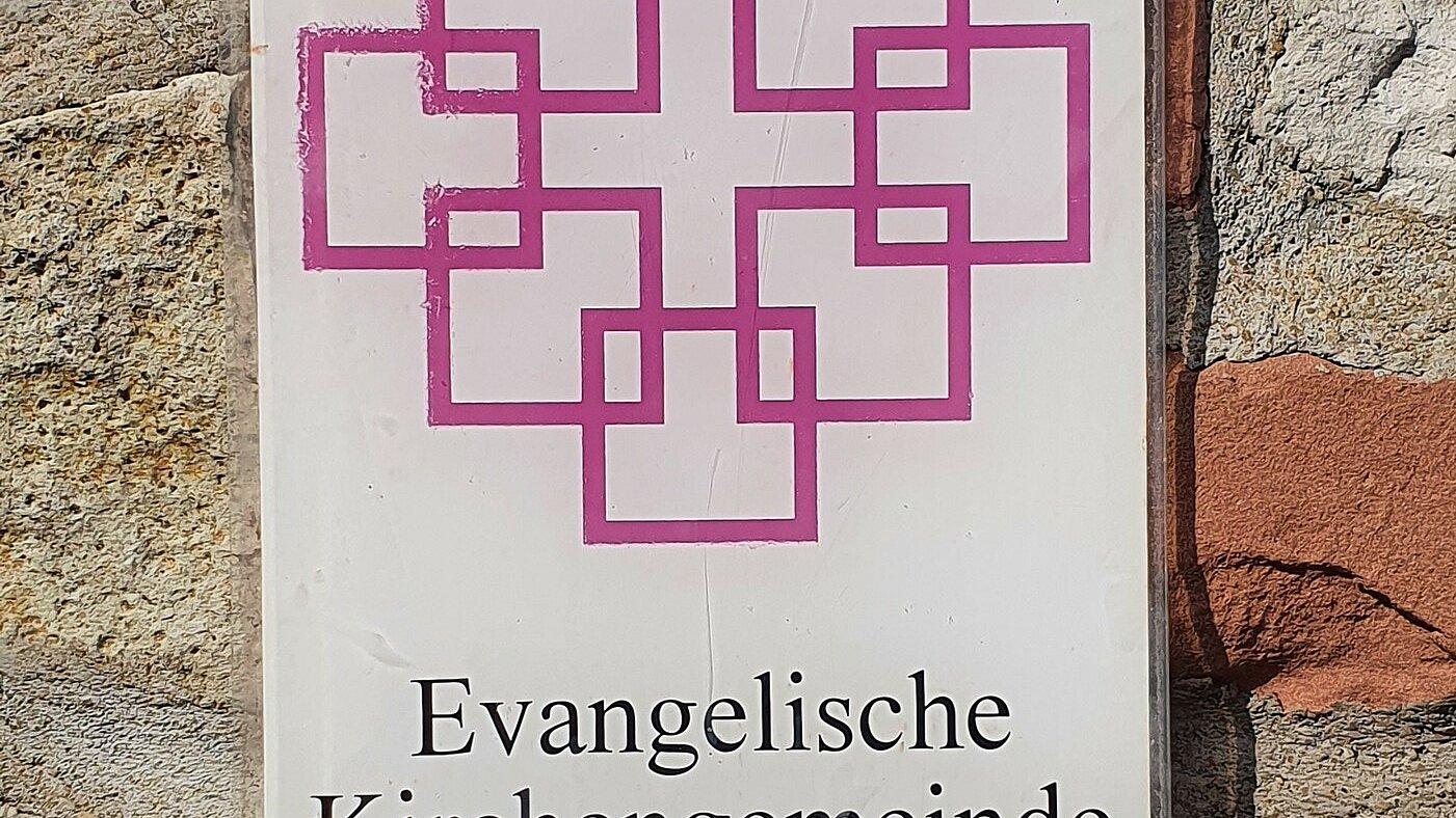Schild Evangelische Gemeinde Ein Schild an der Mauer der Kirche in Middelhagen auf Rügen zeigt das Facettenkreuz der Evangelischen Kirche.