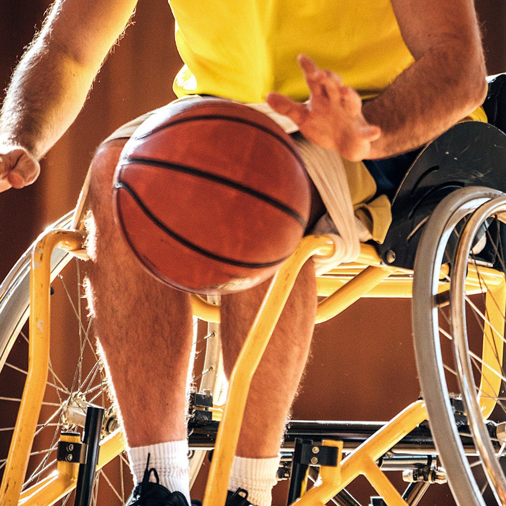 Rollstuhlbasketball- Ausschnitt eines Rollstuhlbasketballer in Aktion - ein Mensch sitzt im Rollstuhl, davor ein ein Basketball