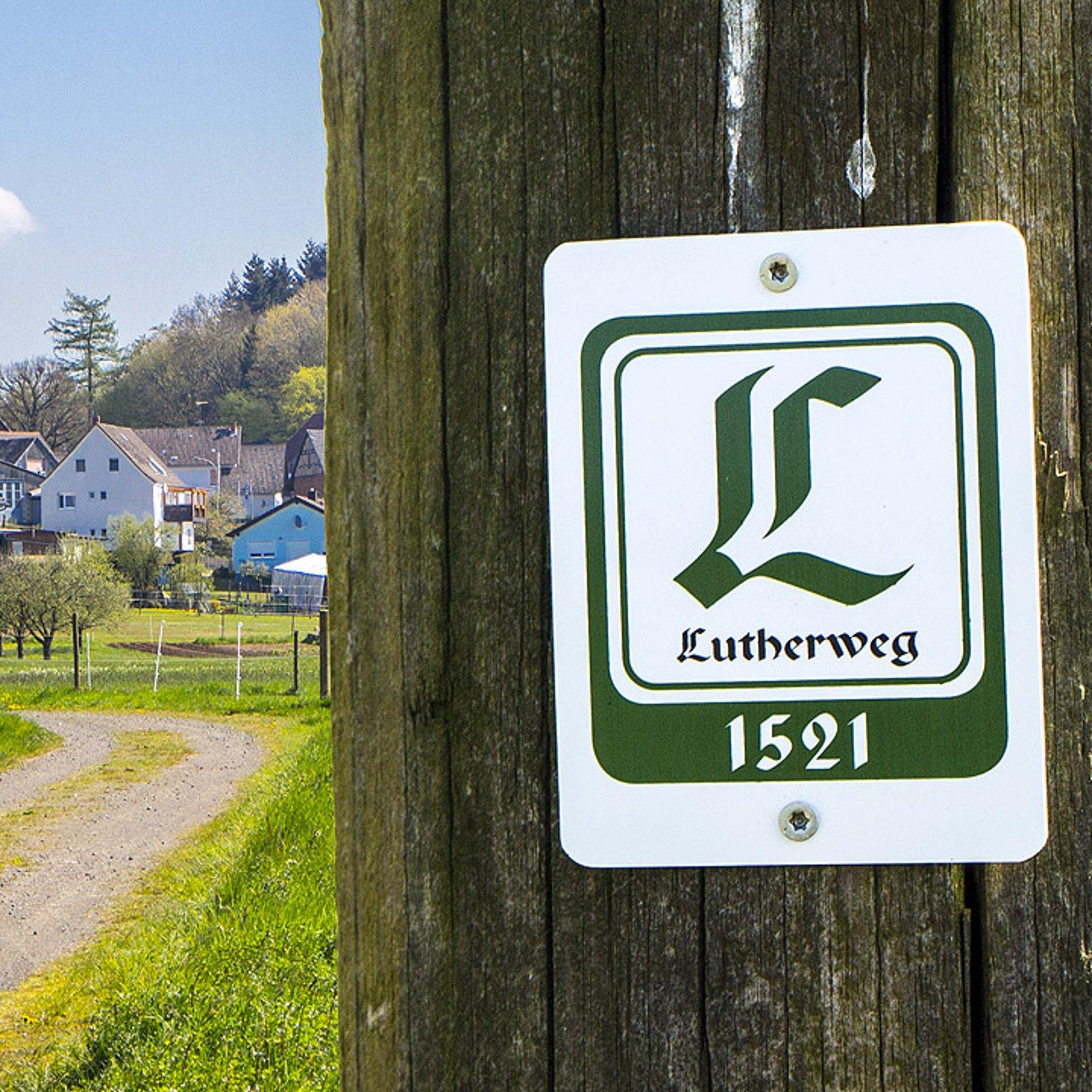 Lutherweg Logo des Lutherweges, dahinter ein Dorf