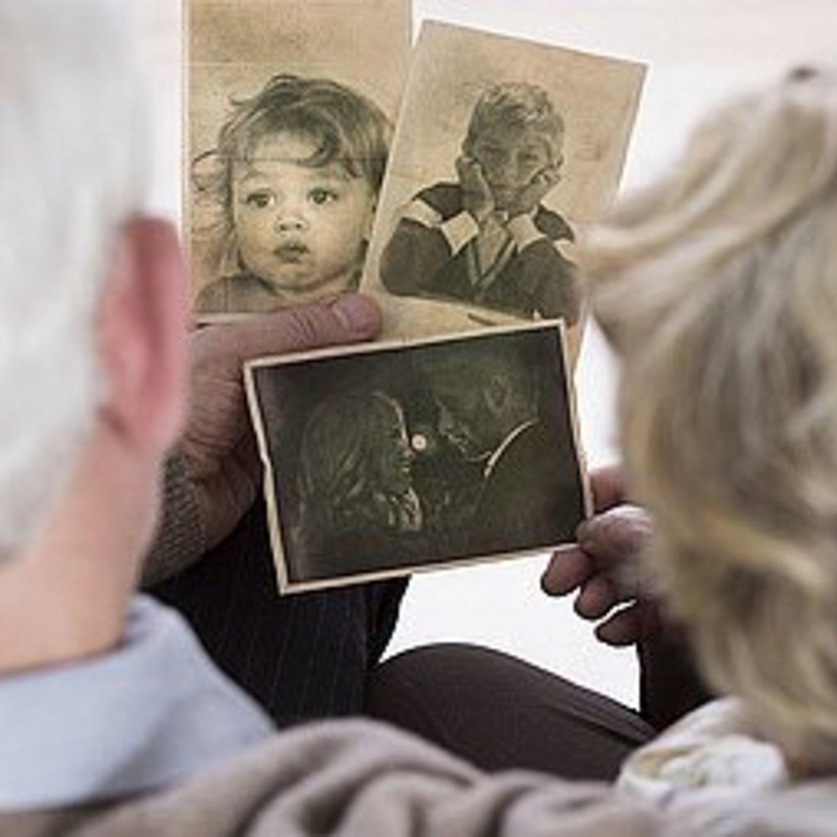 Zwei Senioren schauen auf verschiedene alte Kinderfotos