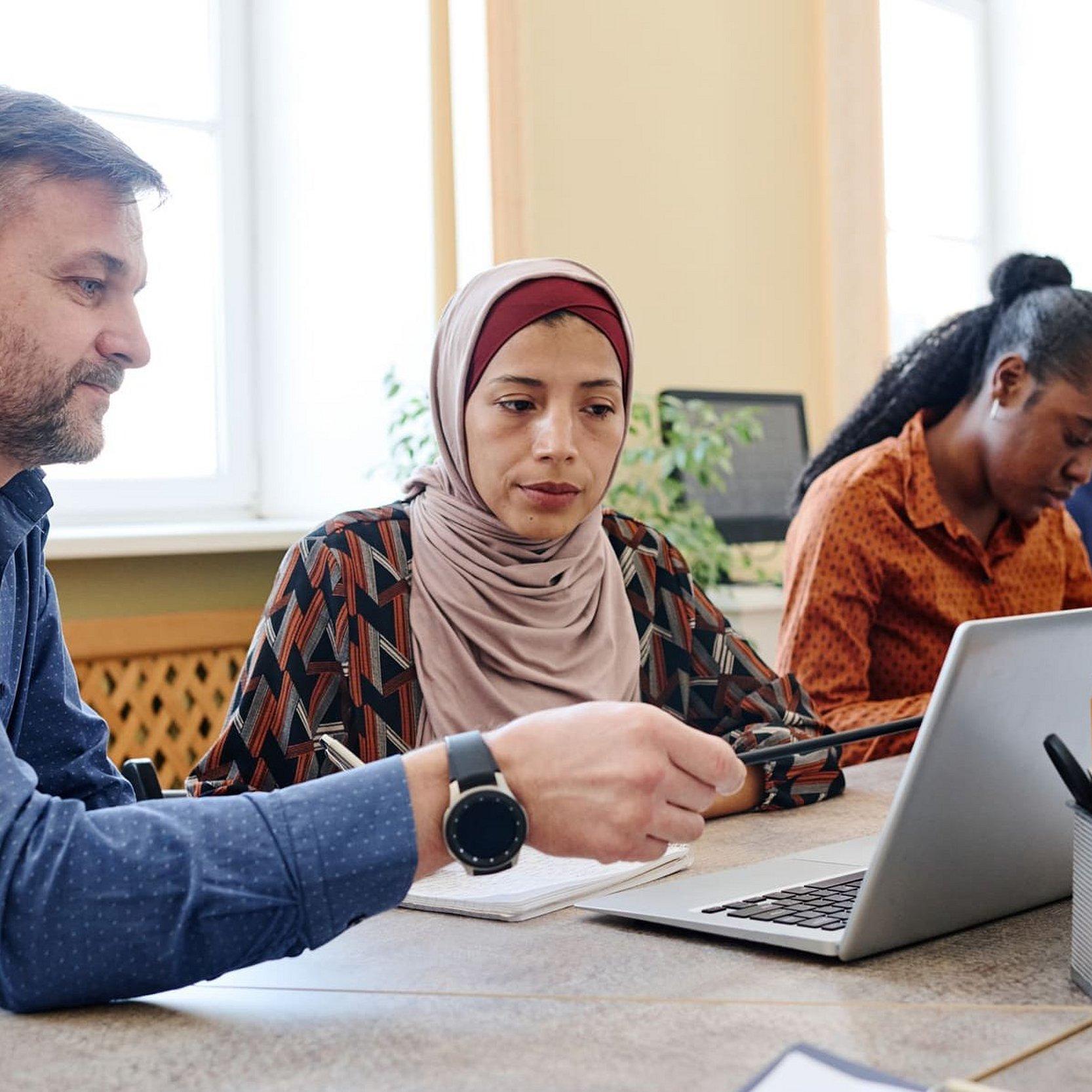 Hilfe für Geflüchtete Ein Mann erklärt einer Frau mit Migrationshintergrund eine Aufgabe an einem Computer