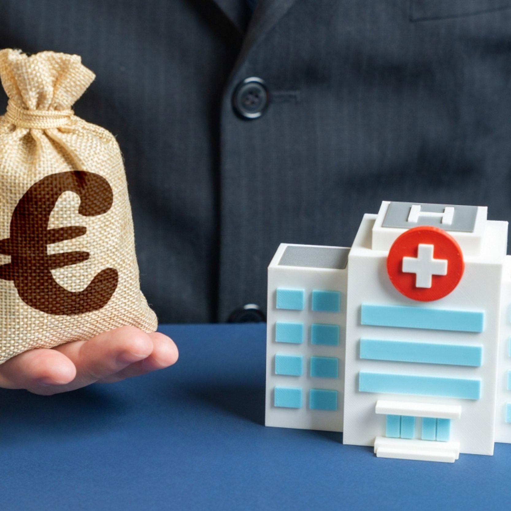 Spenden Krankenhaus Modell eines Krankenhauses und Mann mit kleinem Geldsack, auf dem ein Euro-Zeichen ist