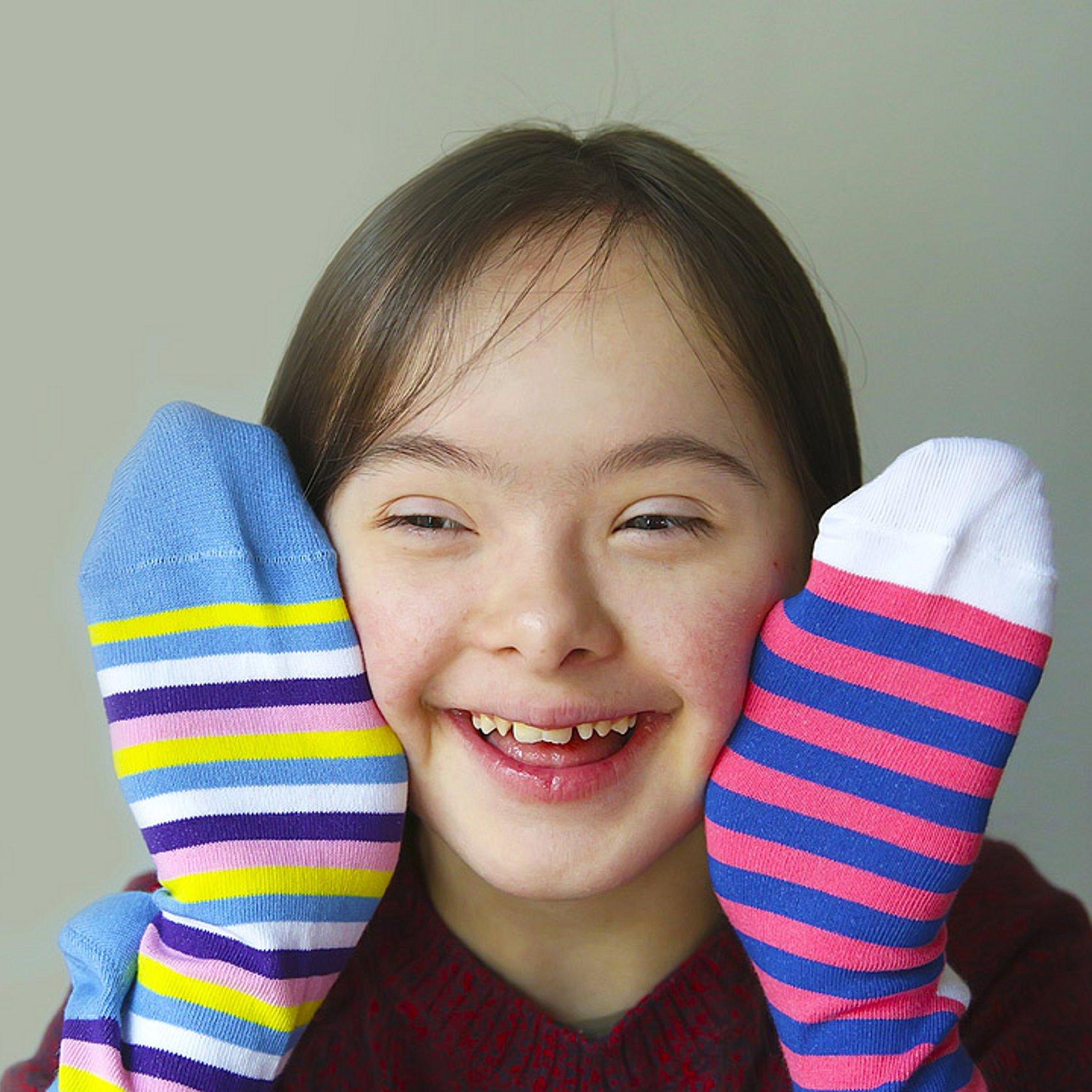 Coole Socke Mädchen mit Downsyndrom hält 2 bunte Socken hoch