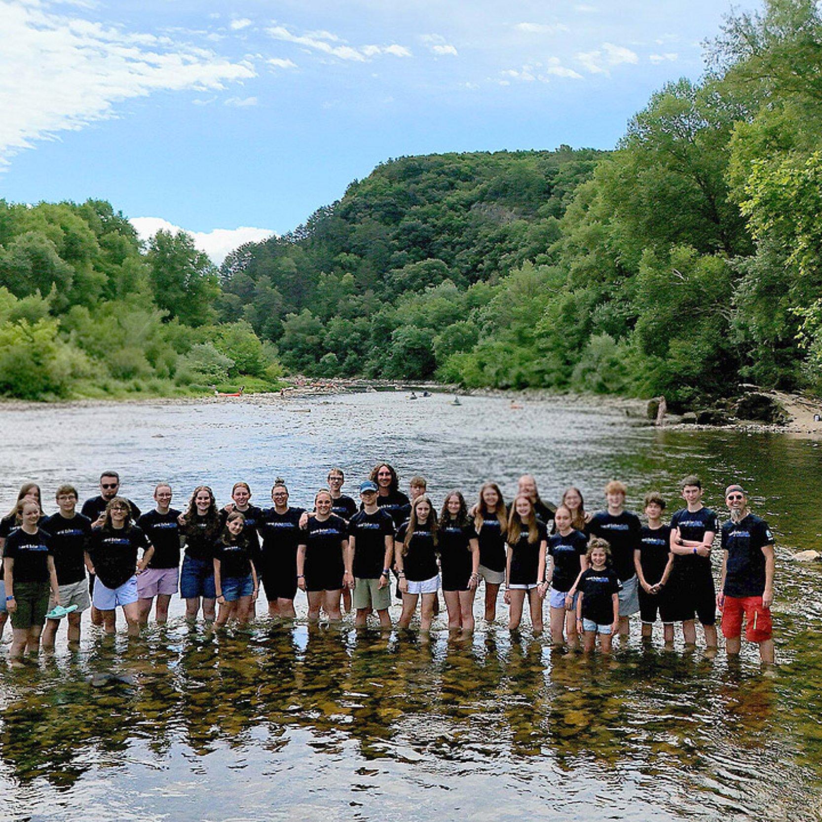 Freizeit Jugendgruppe, die im flachen Wasser eines Flusses steht, dahinter Berge
