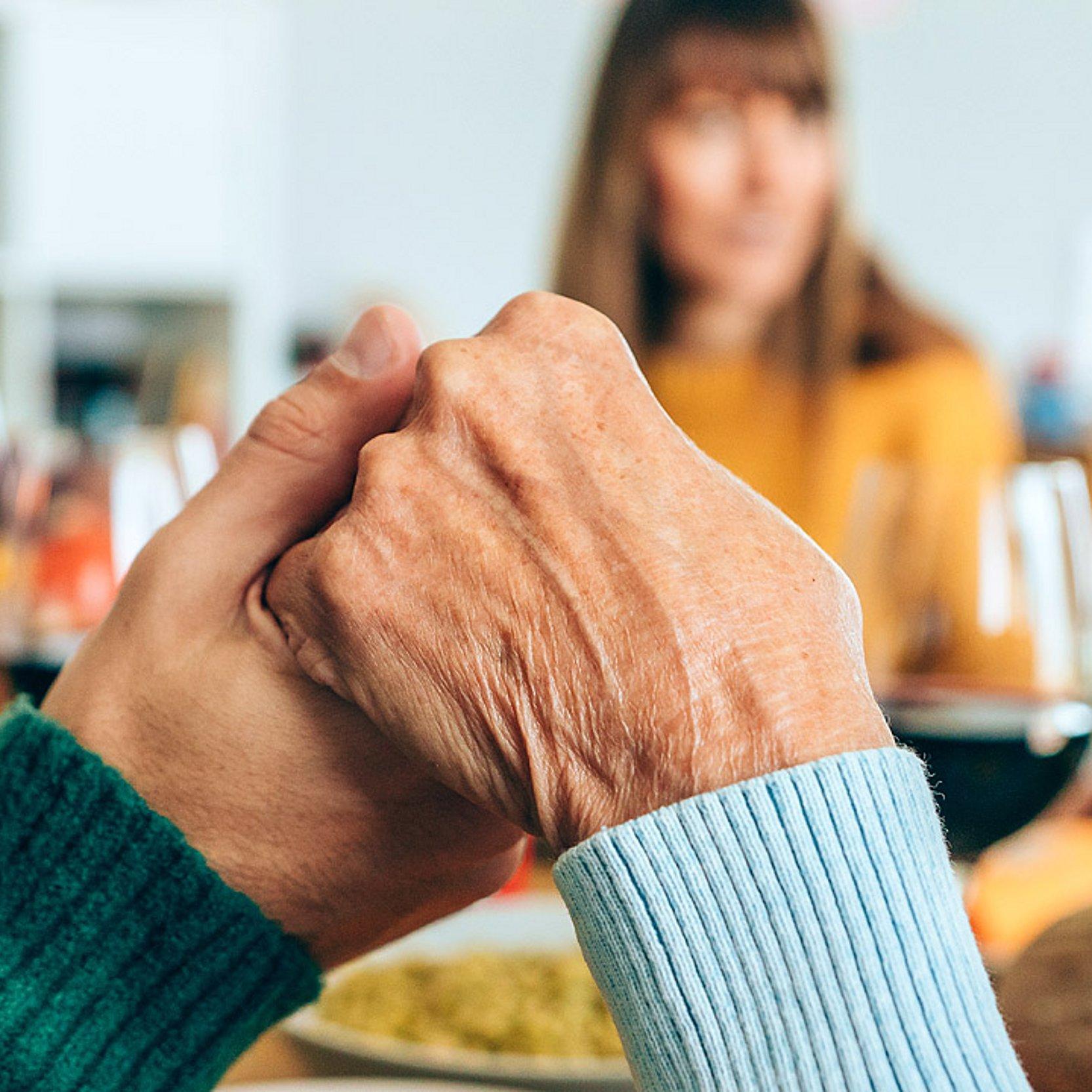 Menschen siten am Tisch und halten sich an den Händen, ihre Augen sind geschlossen