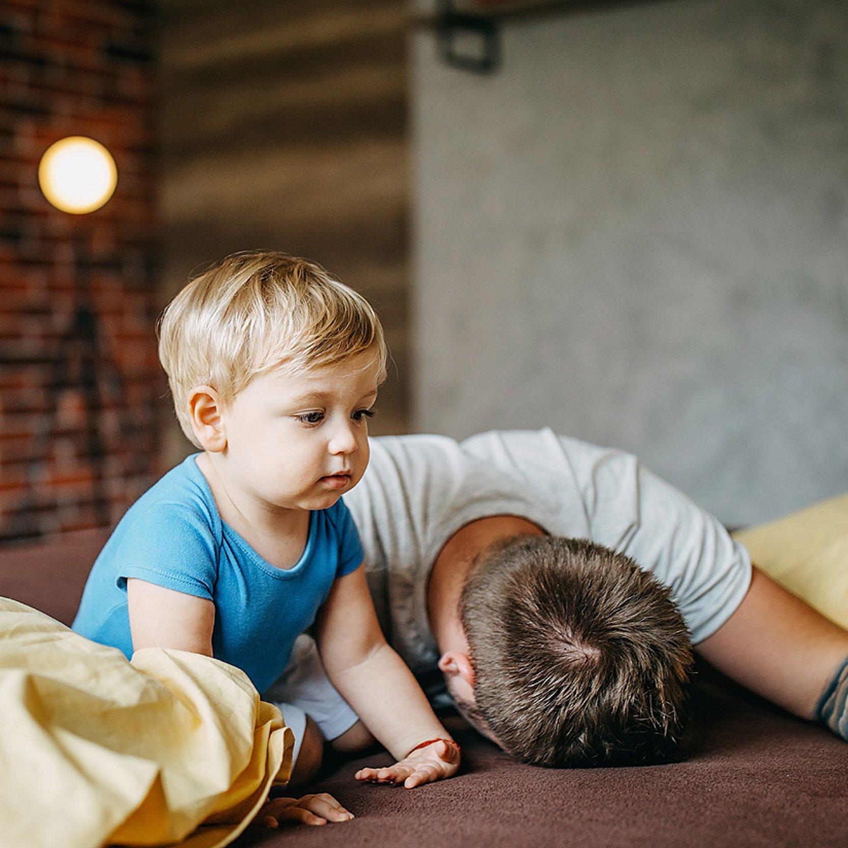 Erschöpfter Vater Kopf eines Vaters liegt auf einem Bett, daneben ein Kleinkind