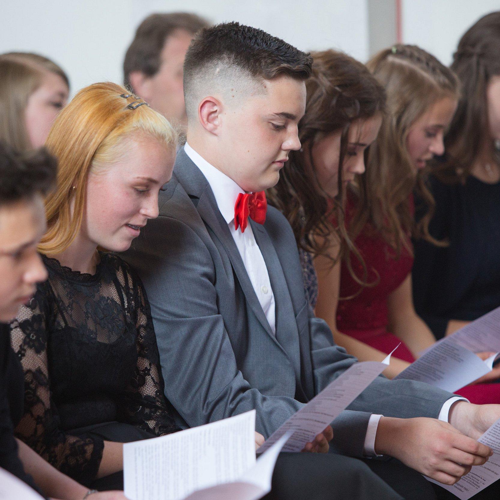 Jugendliche sitzen in einer Kirchenbank und singen