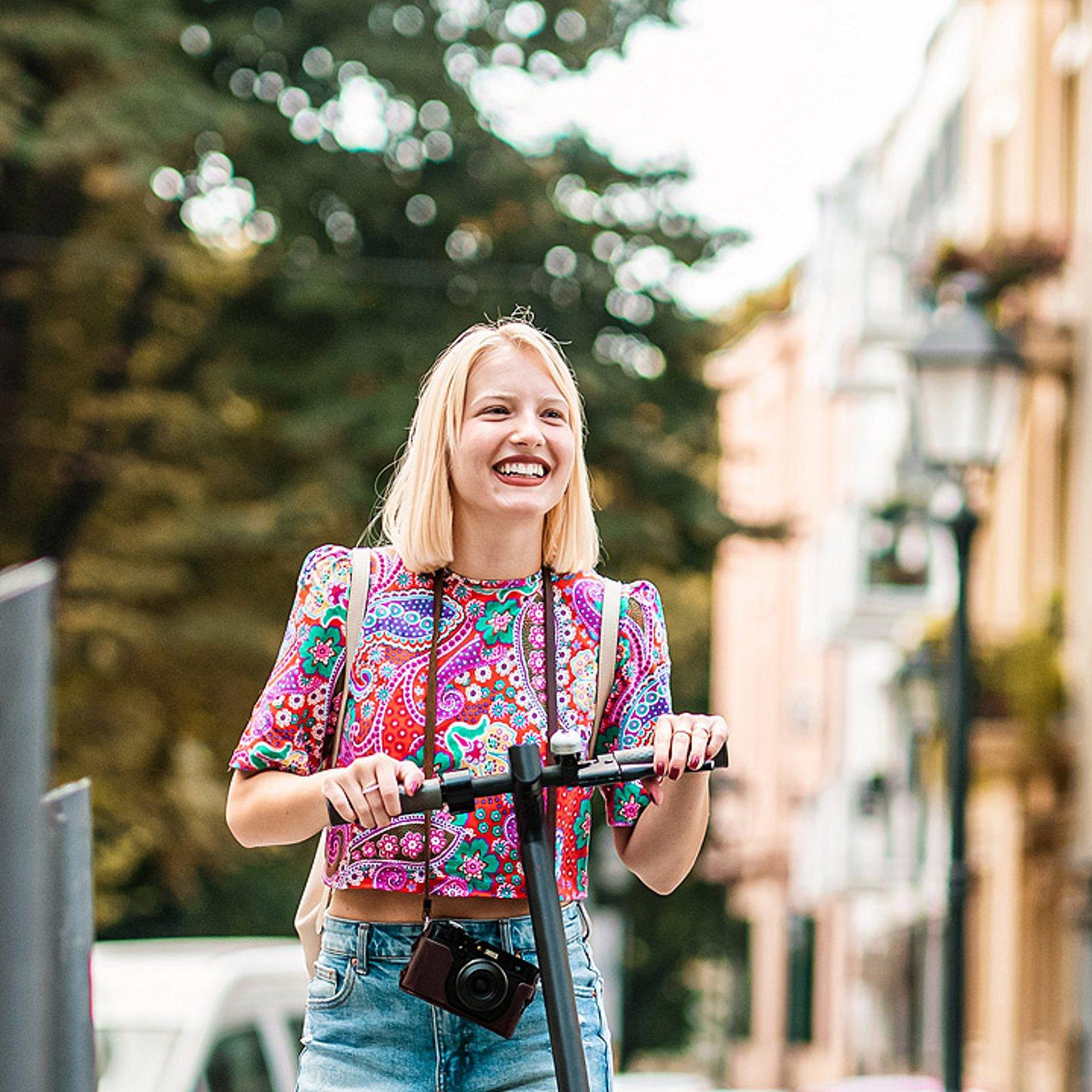 Stadt erkunden Eine Frau mit einem Roller erkundet die Stadt