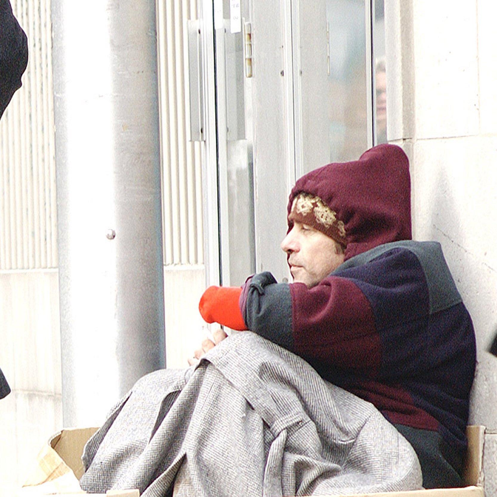 Obdachloser Obdachloser Mann sitzt im Winter in einer Fußgängerzone, Menschen eilen vorbei