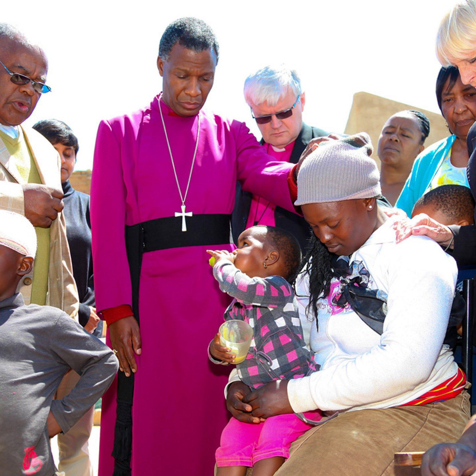 Ein Preises, ein Erzbischof, stehen zwischen ein paar Menschen, sie beten miteinander