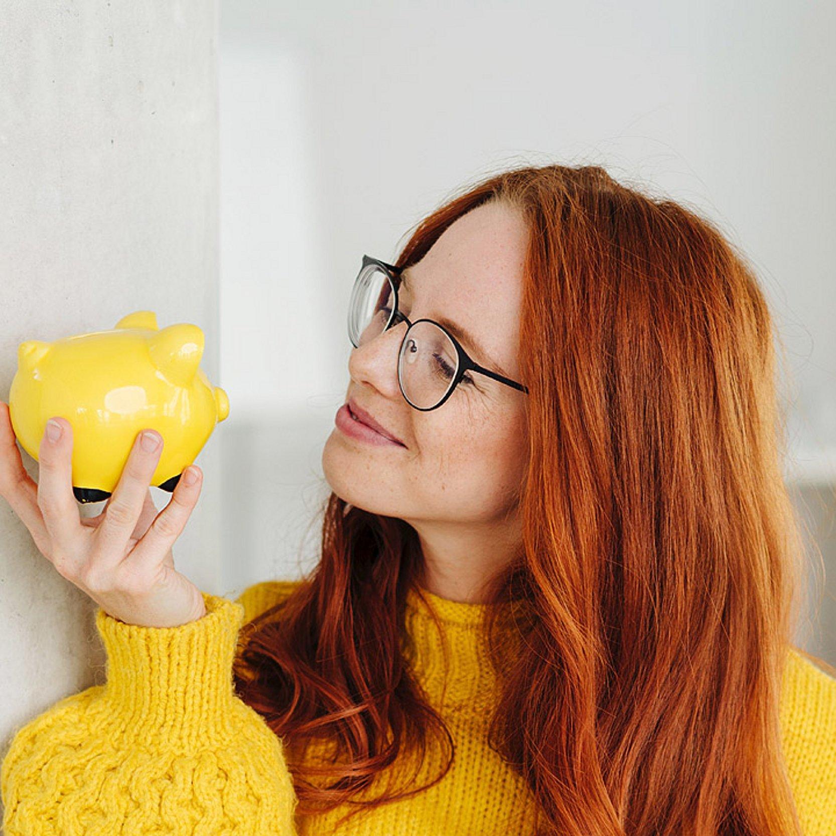 Sparen Eine Frau hält ein gelbes Sparschwein in der Hand und lächelt es an