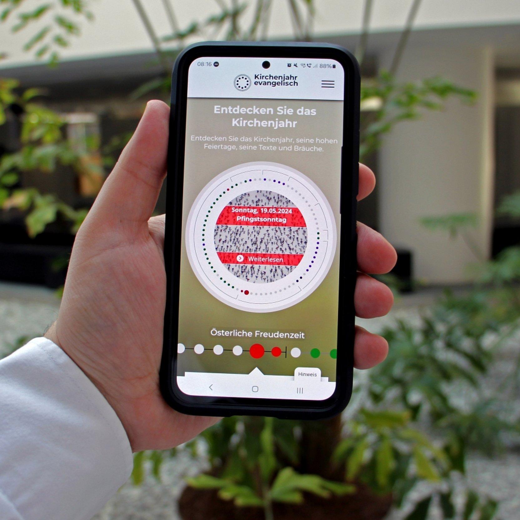 Smartphone App Kirchenjahr 2024 Jemnad hält ein Smartphone in der Hand, es ist die App zu sehen.