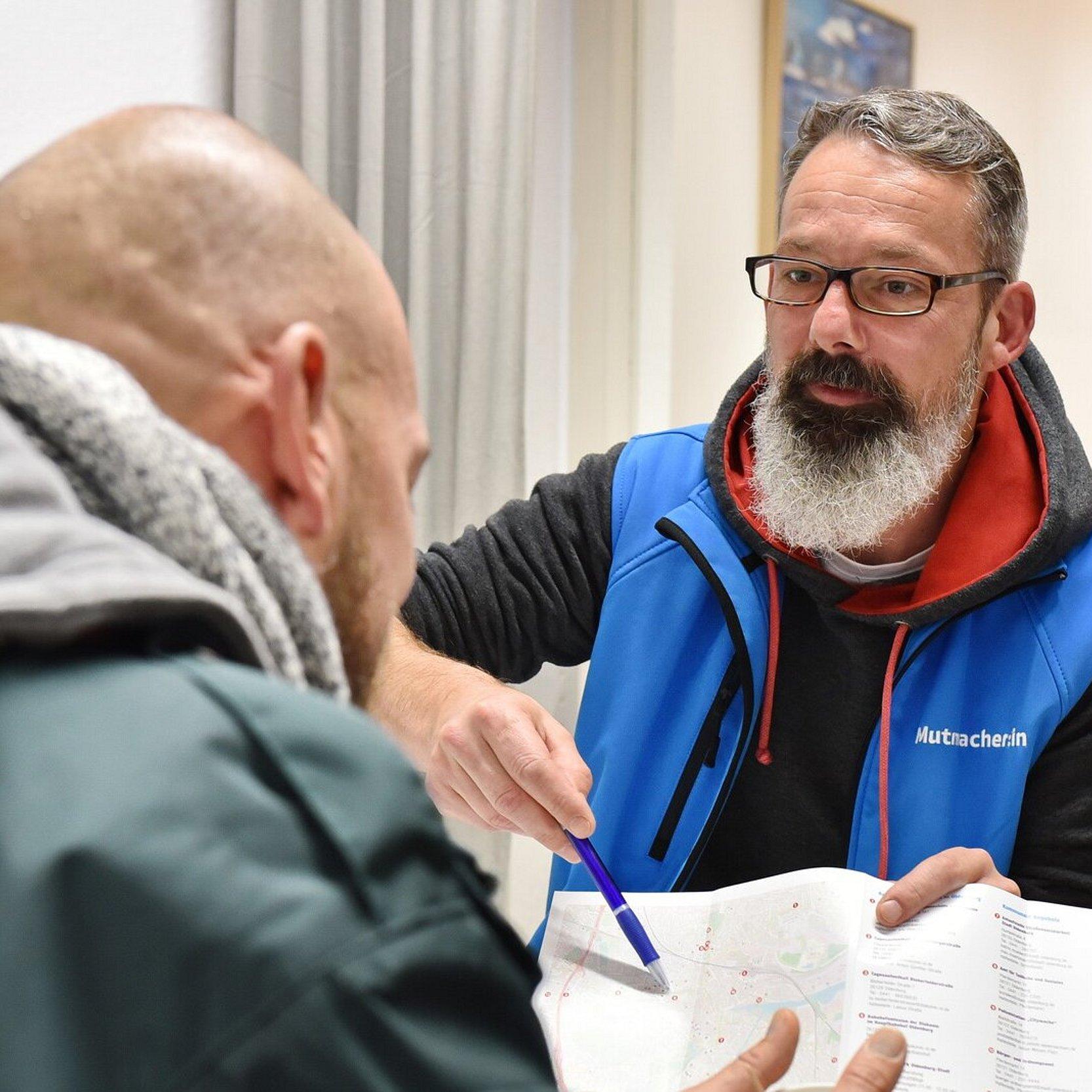 Beratung in der Bahnhofsmission Mitarbeiter der Bahnhofsmission im Beratungsgespräch. Mitarbeiter zeigt Klienten eine Broschüre oder Karte.