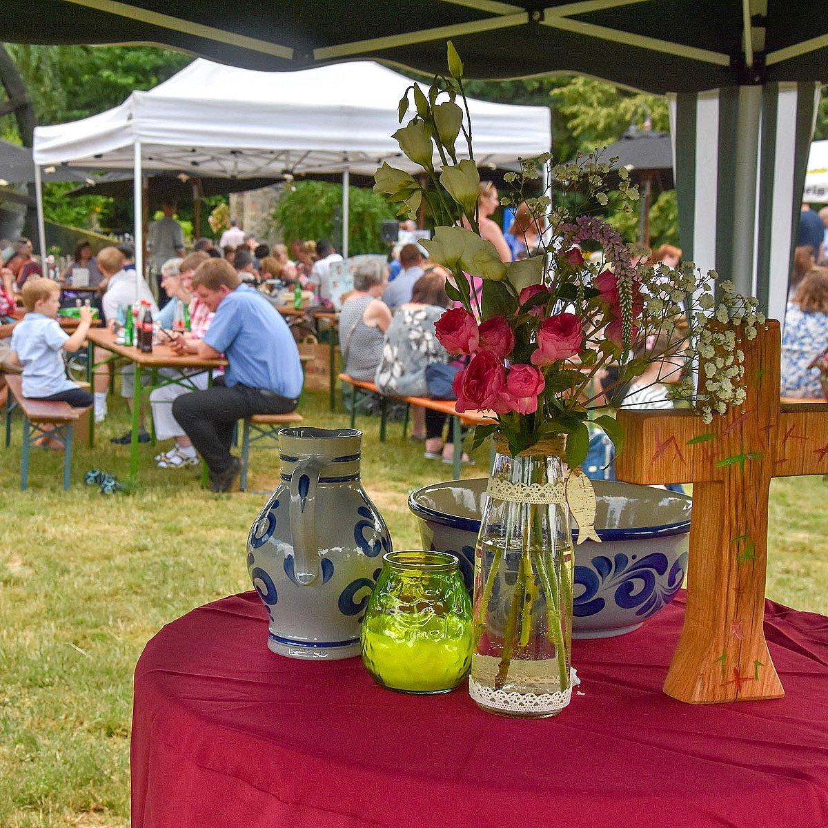 Tauffest Menschen auf Bierbänken, davor ein Freiluft-Altar