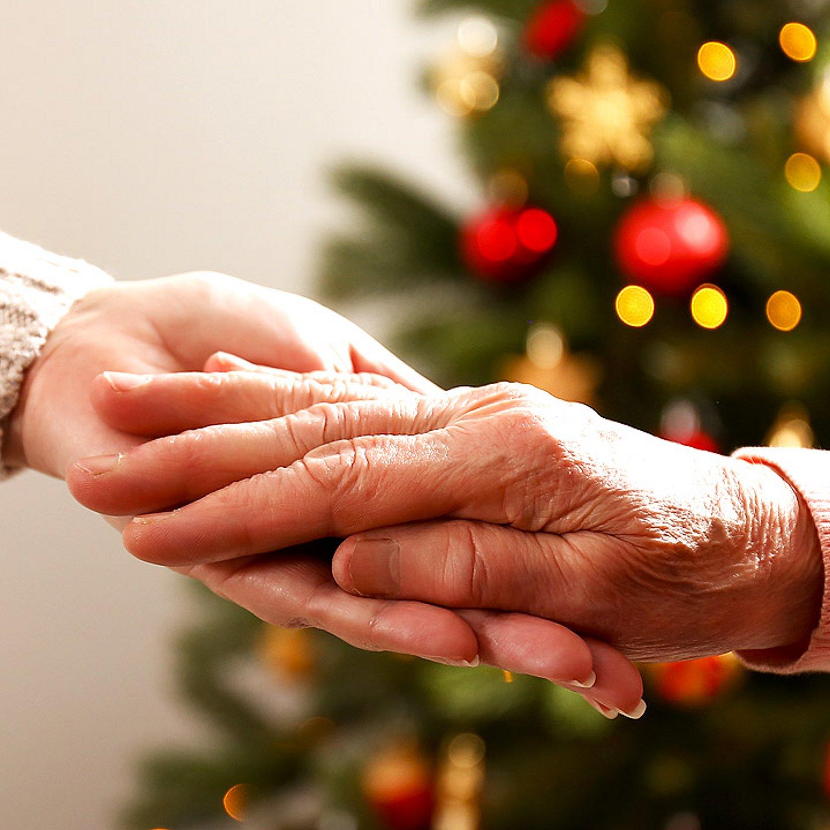 Beistand im Advent Eine Hand hält die Hand einer älteren Dame, dahinter ein geschmückter Weihnachtsbaum