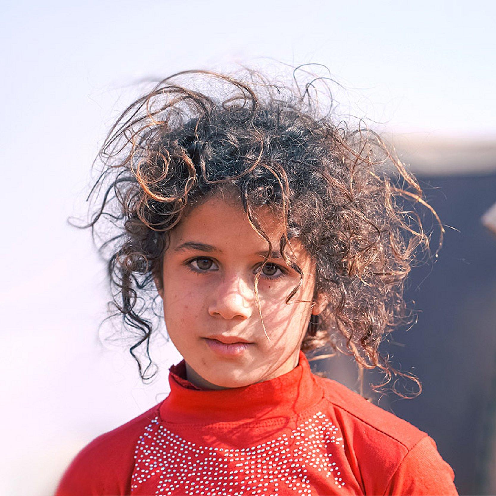 Kind Ein Kind mit etwas zerzausten Haaren, im Hintergrund eine Art Zelt