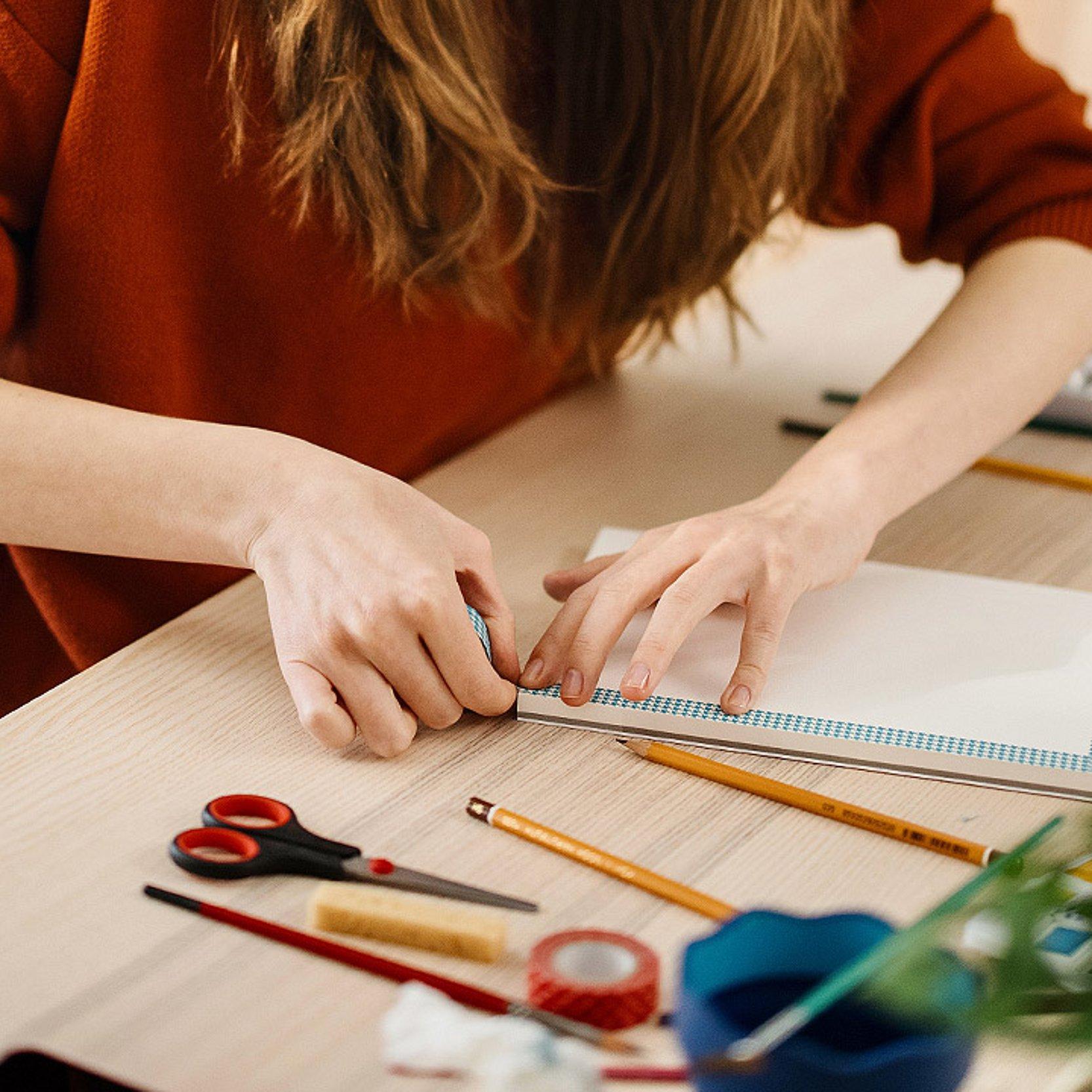 Kunst Hände einer Frau berühren Aquarellpapier, daneben liegen Stifte