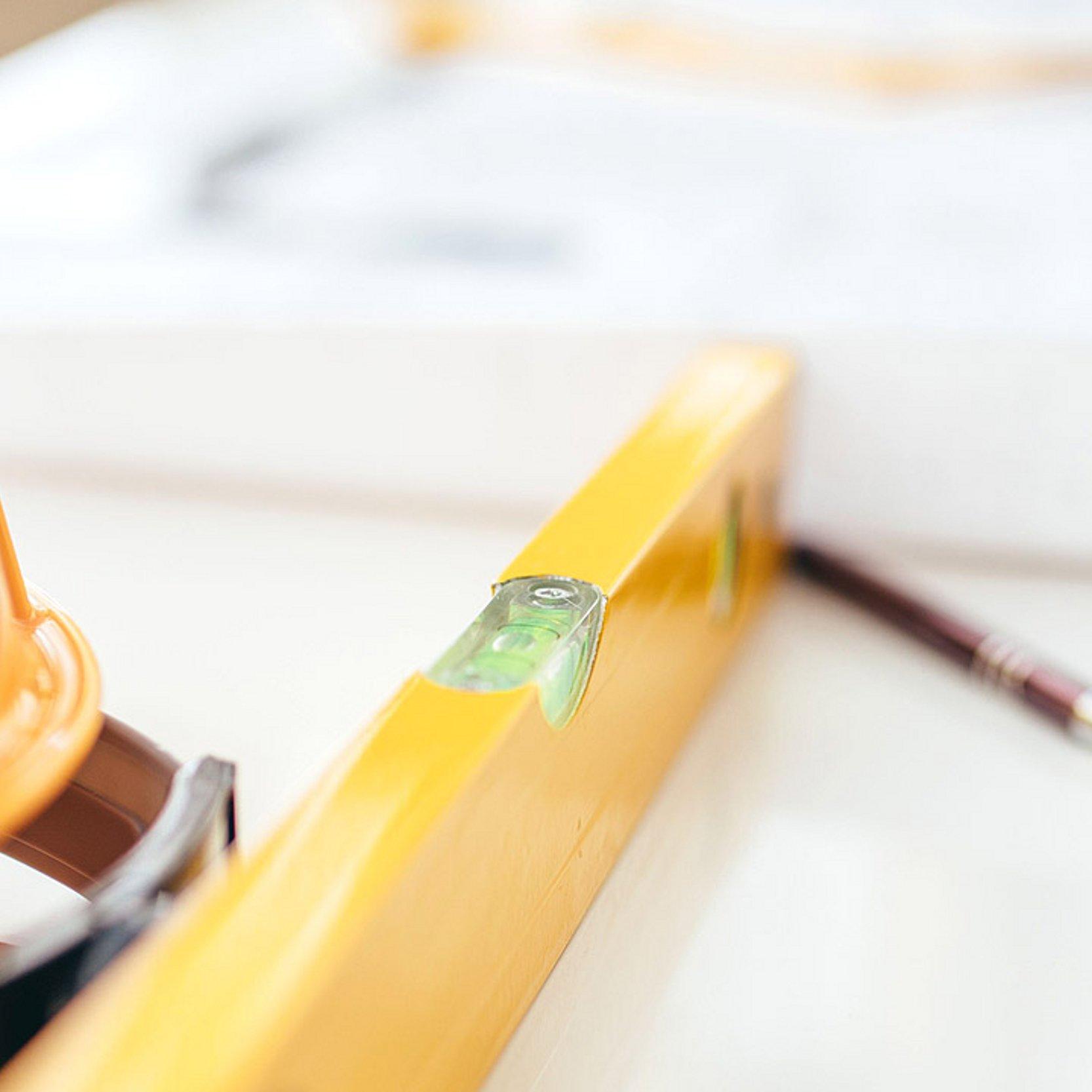 Bauen Gelber Schutzhelm und eine Wasserwaage auf einem Tisch