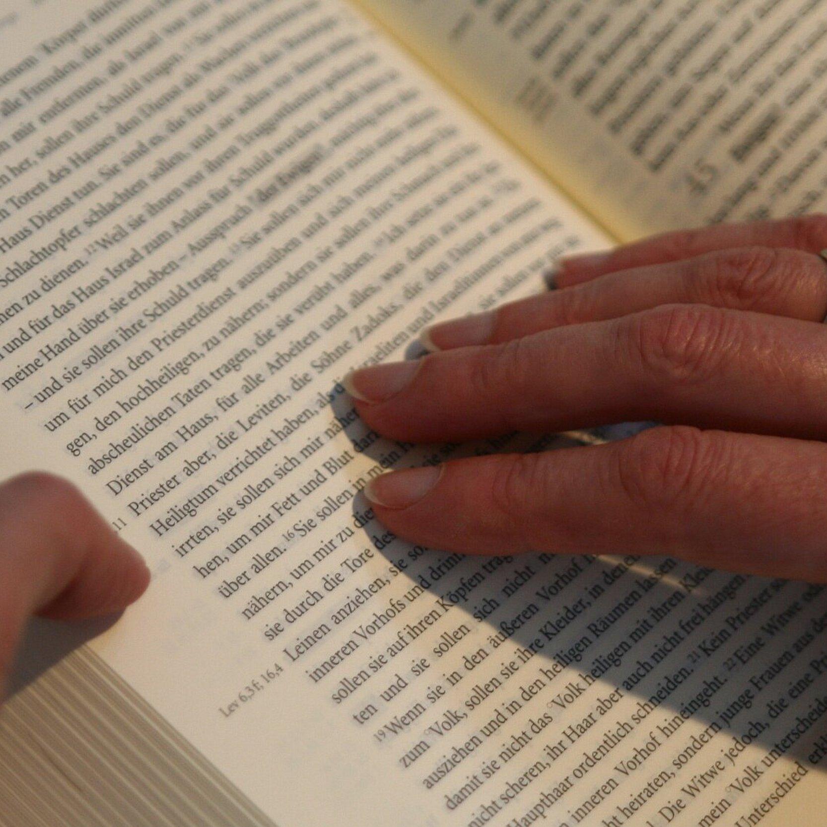 Eine Hand ruht auf einer aufgeschlagenen Bibel und verharrt auf einem Satz.