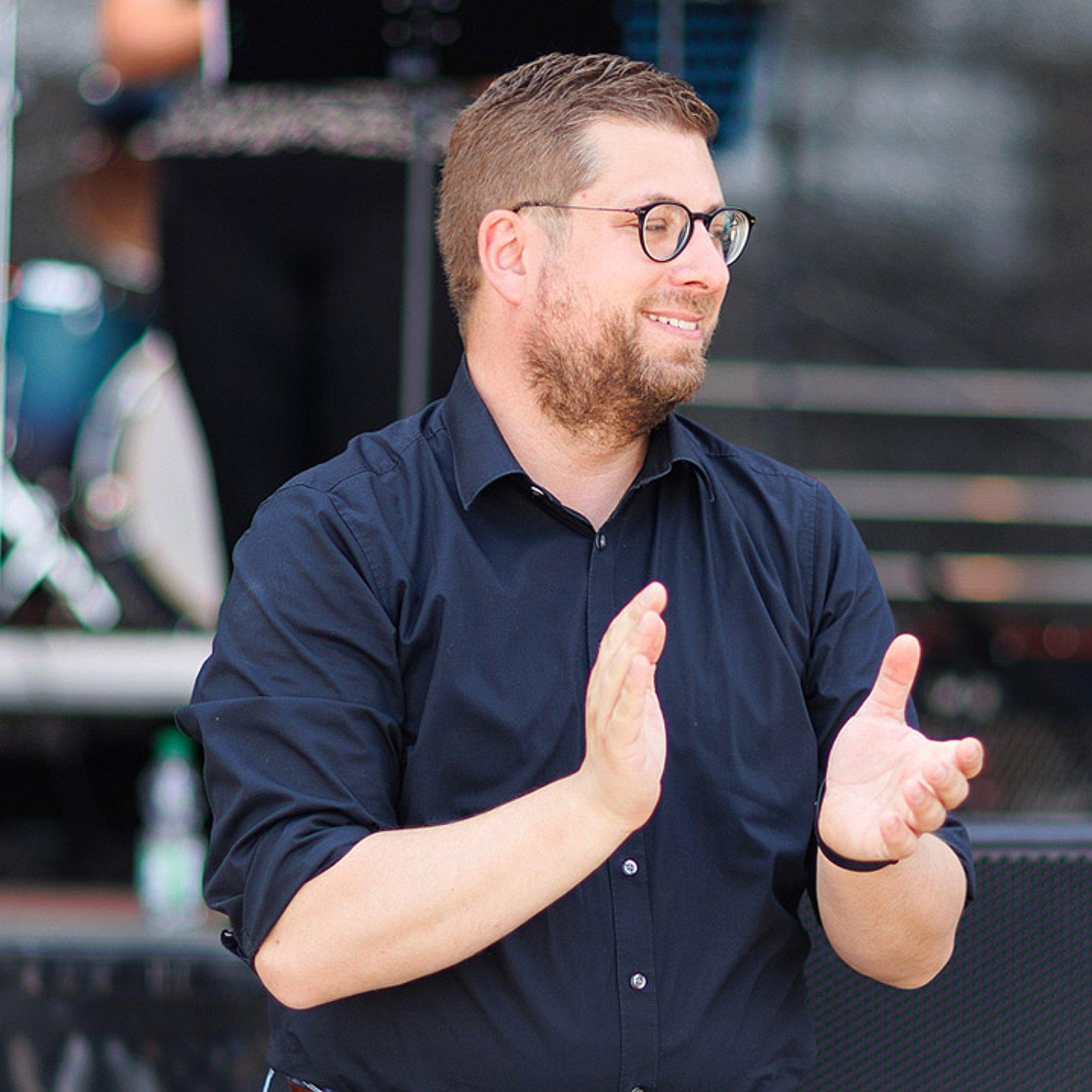 Jörg Niesner Man sieht den Sinnfluencer und Pfarrer Jörg Niesner vor der Bühne beim Jugendkirchentag, im Hintergrund eine Band auf der Bühne